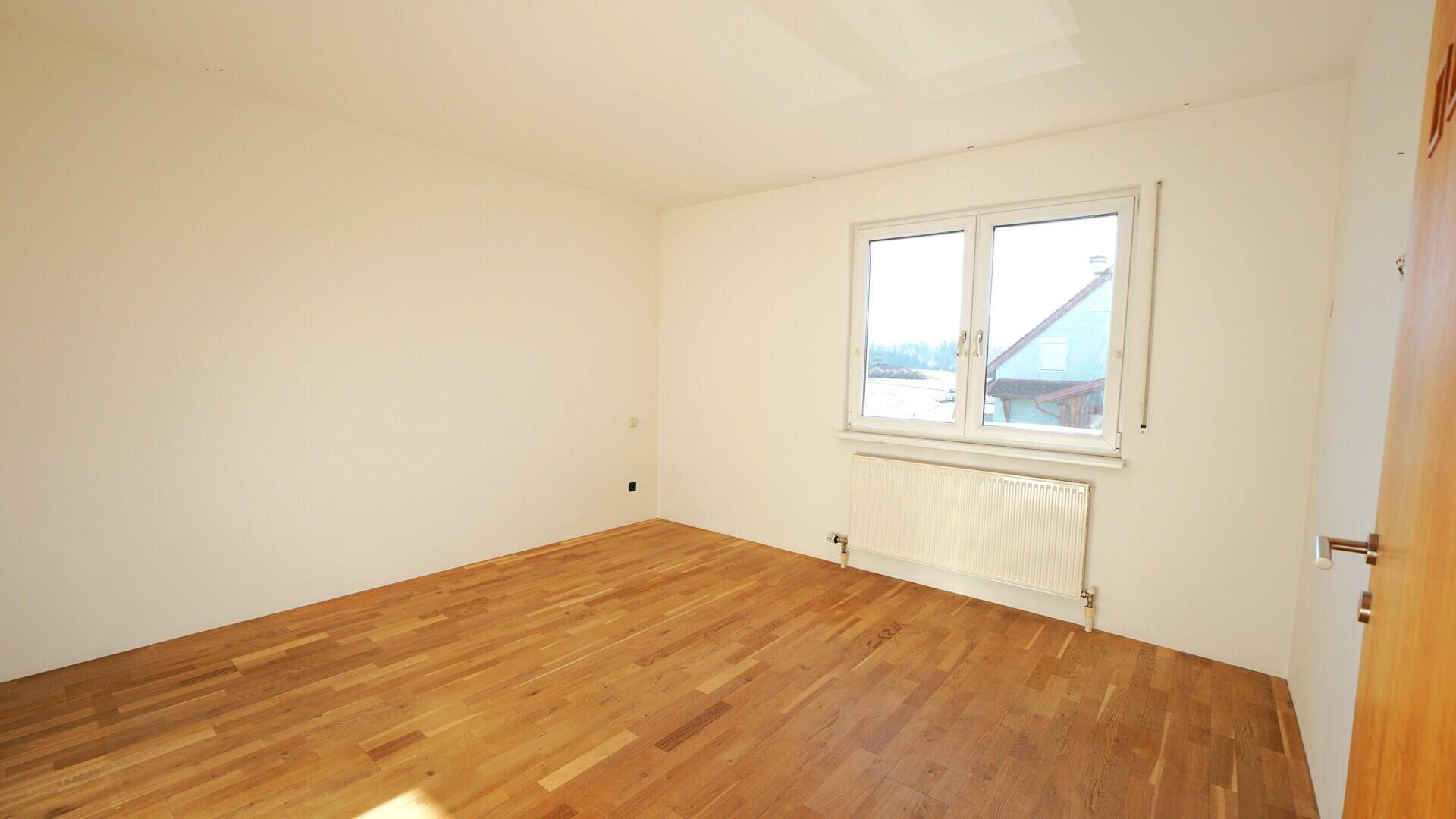 Helles Schlafzimmer mit Parkettboden und großem Fenster, bereit zur individuellen Gestaltung.