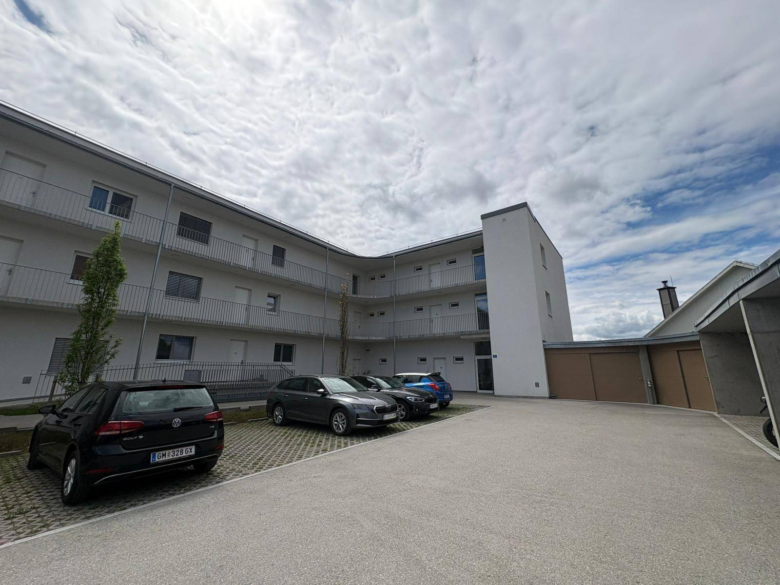 Modernes Mehrfamilienhaus mit Balkonen, Parkplätzen und Garagen unter bewölktem Himmel.