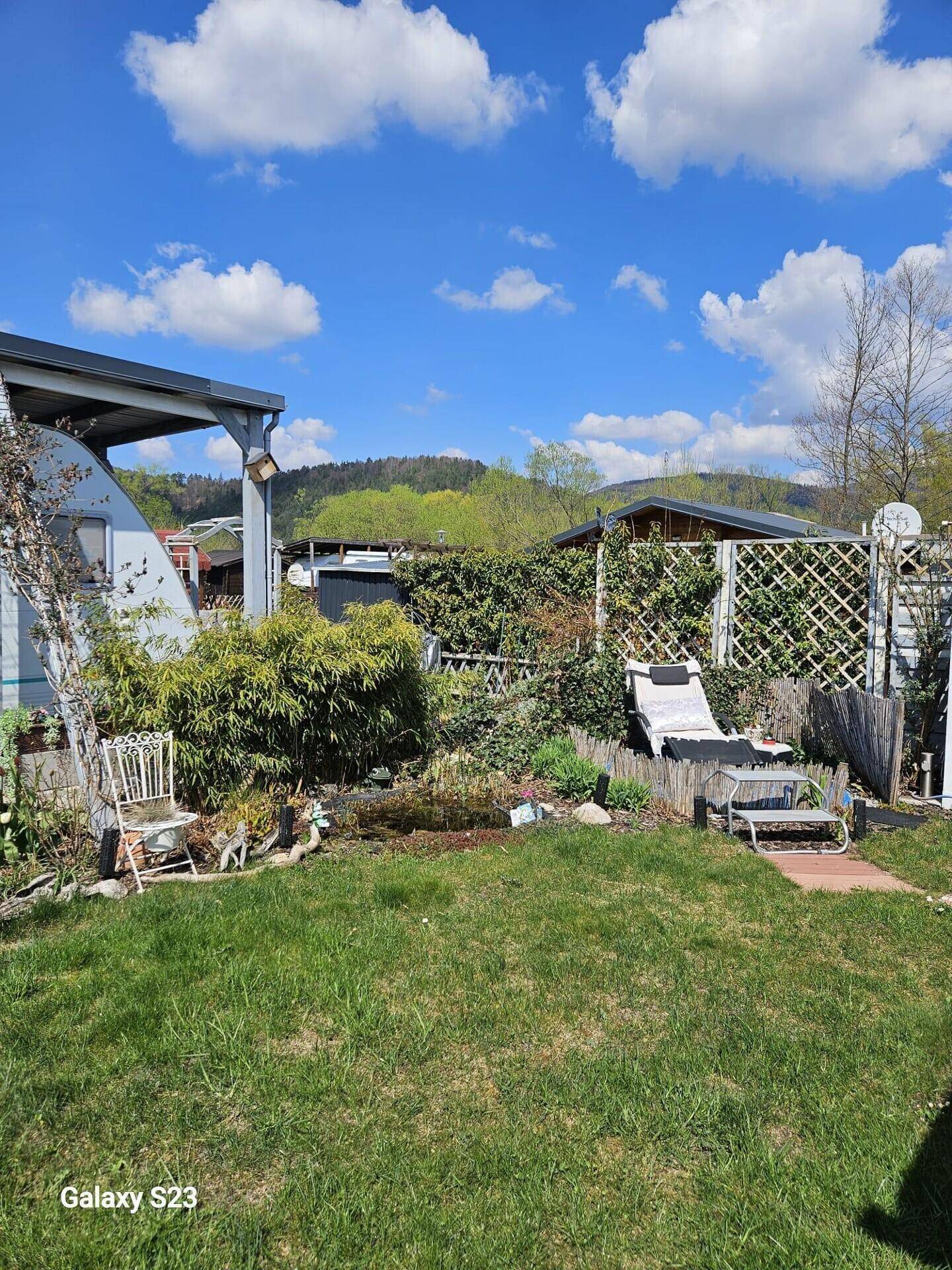Grüner Gartenbereich mit Liegestuhl, Rasenfläche und Blick auf bewaldete Hügel.