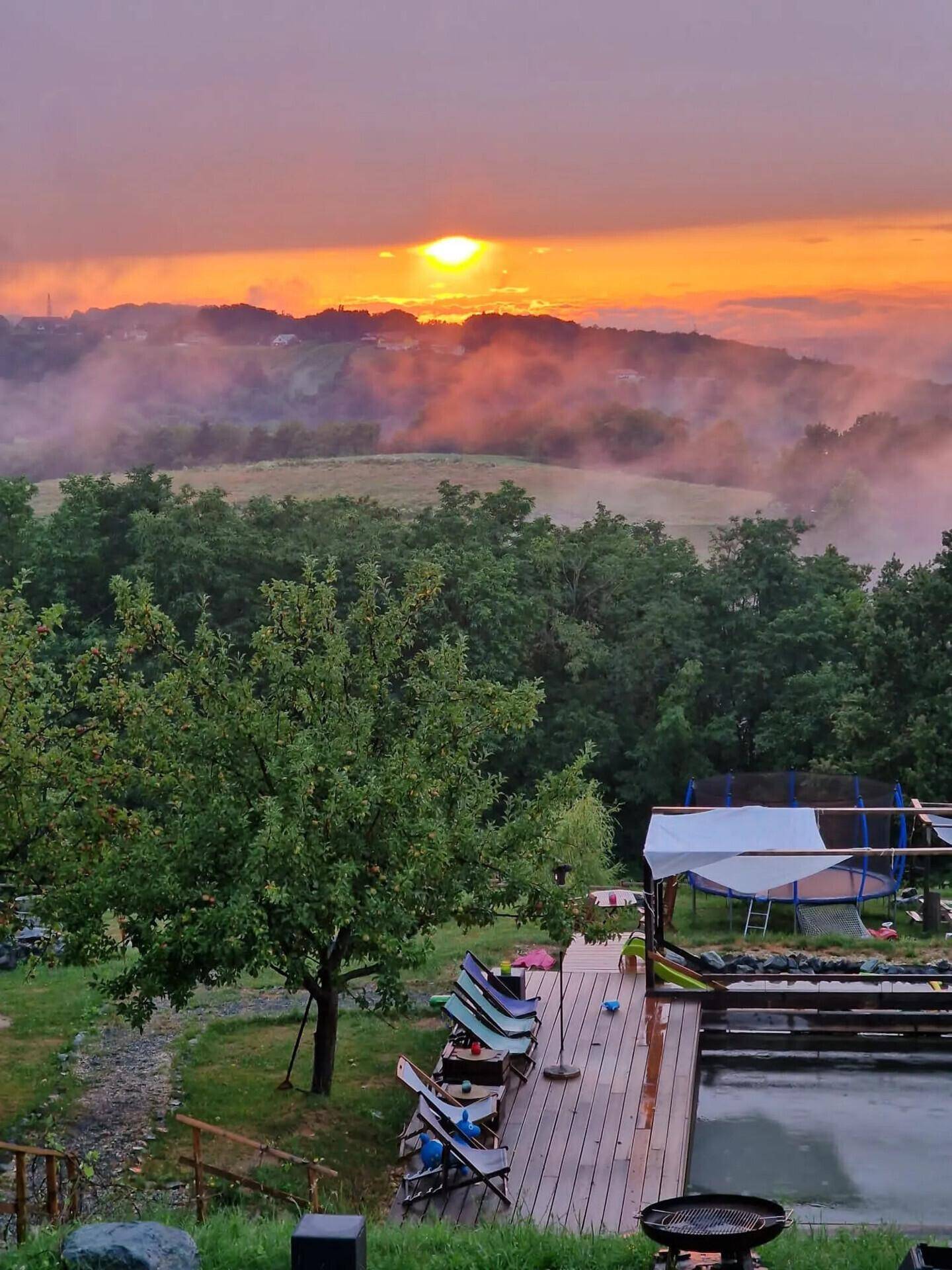 Gartenbereich mit Pool, Trampolin und Liegestühlen bei einem stimmungsvollen Sonnenuntergang.