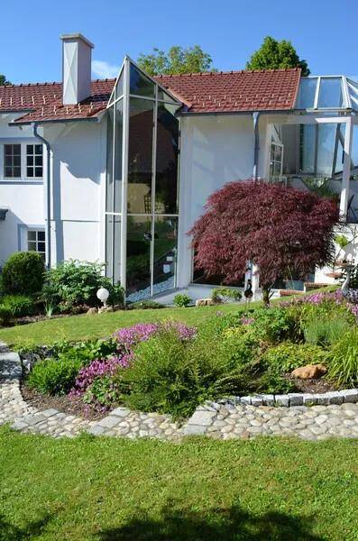 Großzügiger Garten mit Rasenflächen, Blumenbeeten und einem modernen Glasanbau am Haus.