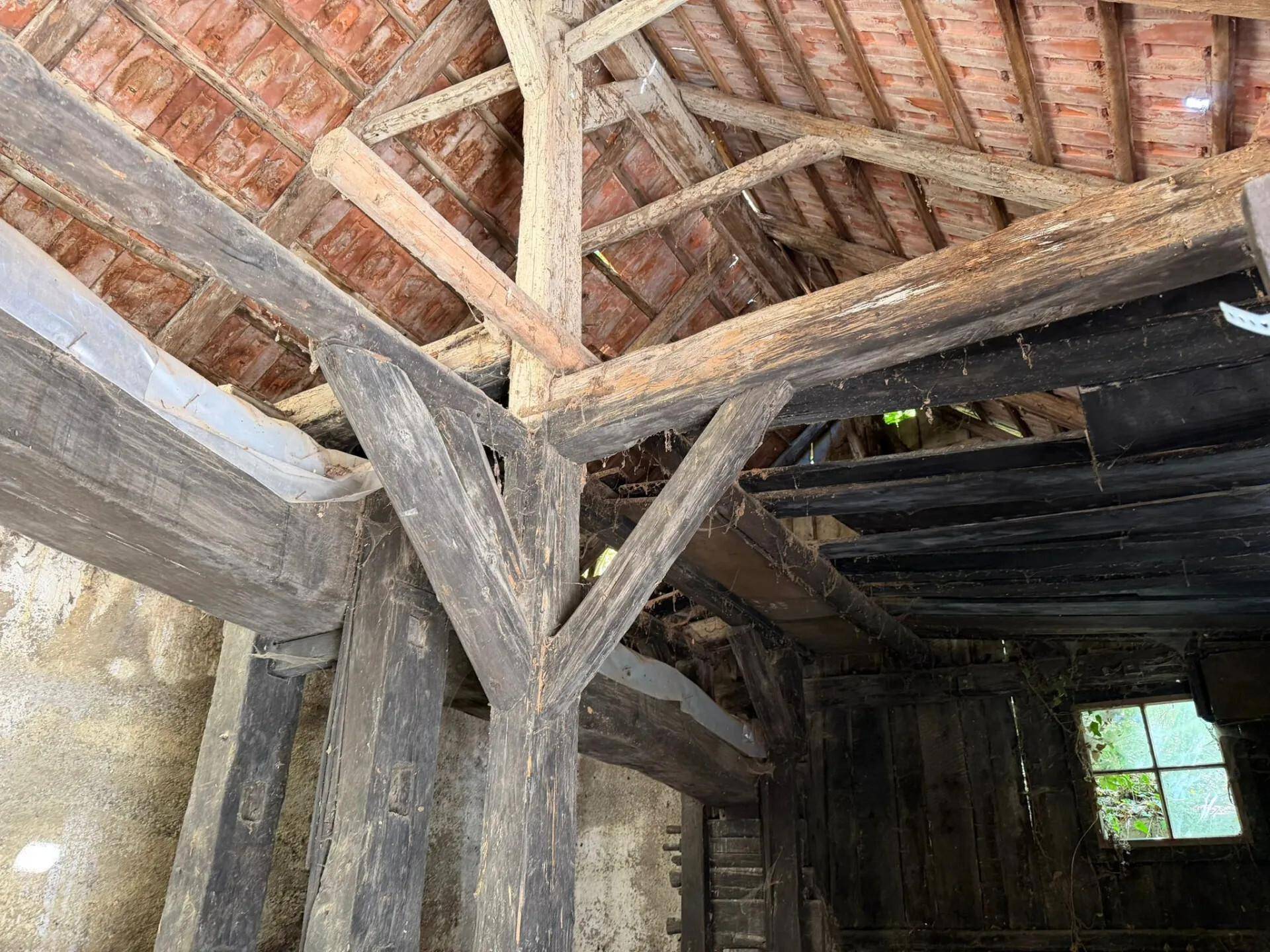 Komplexes Geflecht aus alten Holzbalken, die das Dach eines verfallenen Scheunengebäudes stützen.
