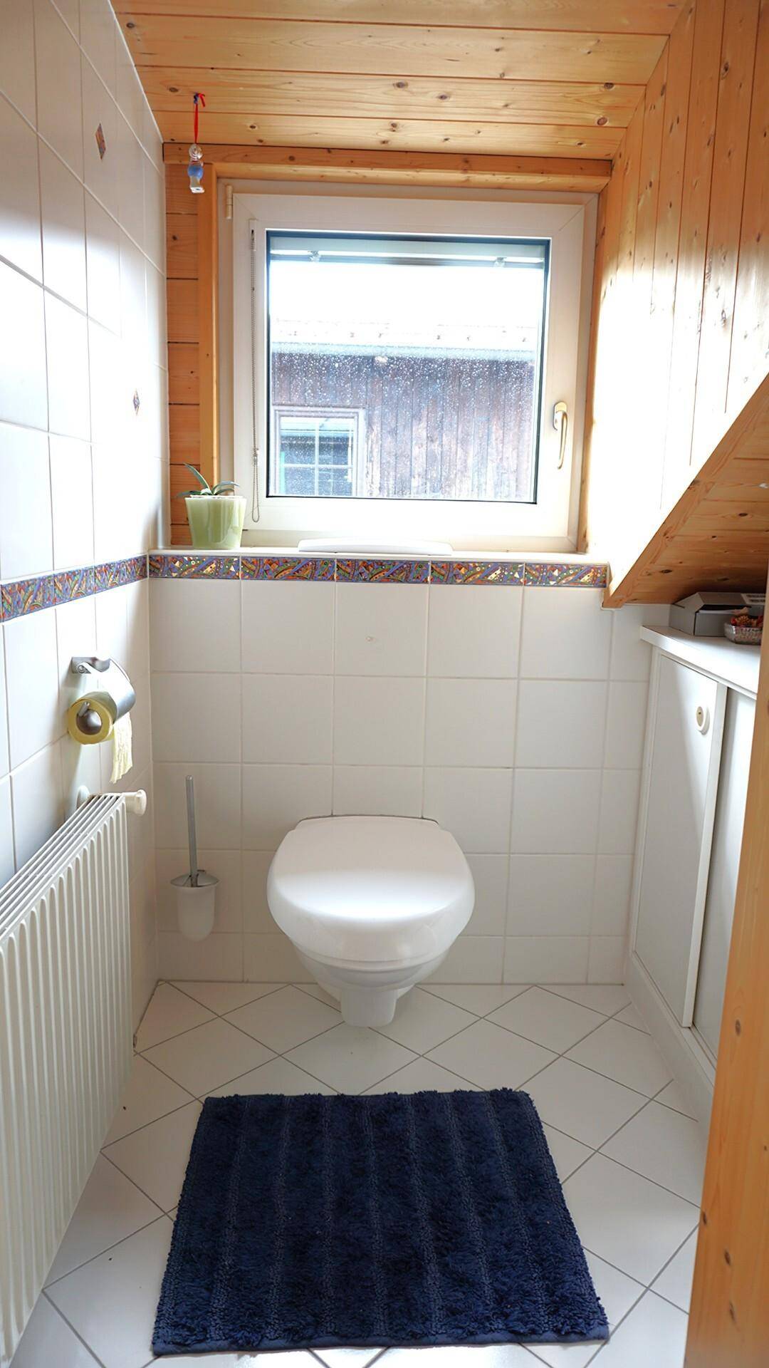 Separate Toilette mit Fenster, weißen Fliesen und Holzdecke.