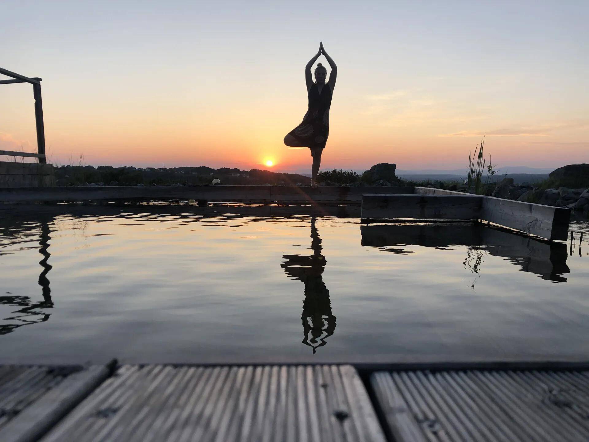 Eine Person macht Yoga am Pool bei einem wunderschönen Sonnenuntergang über der Landschaft.