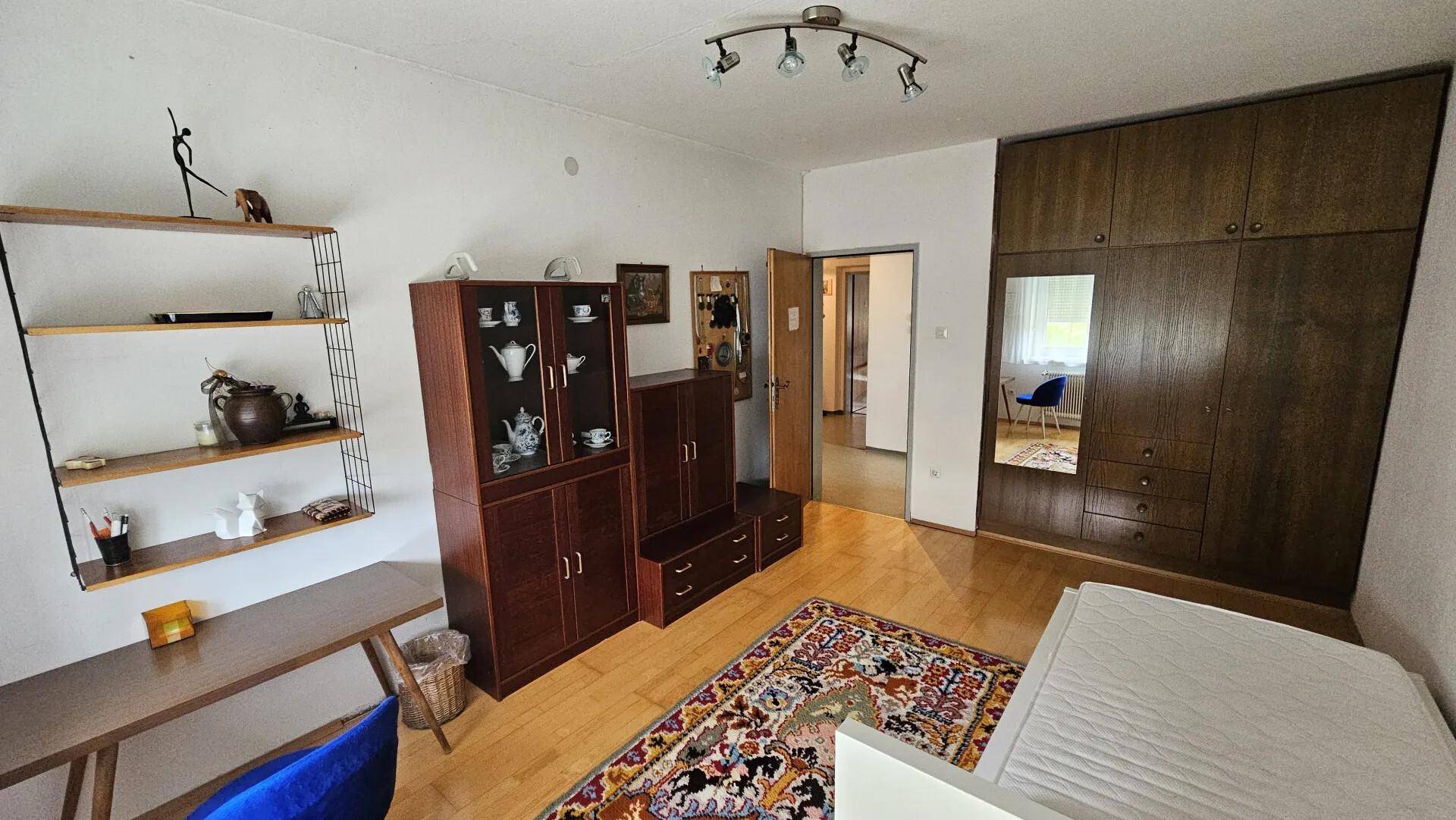 Schlafzimmer mit Einzelbett, großem Holzschrank und Schreibtisch, bietet viel Stauraum.