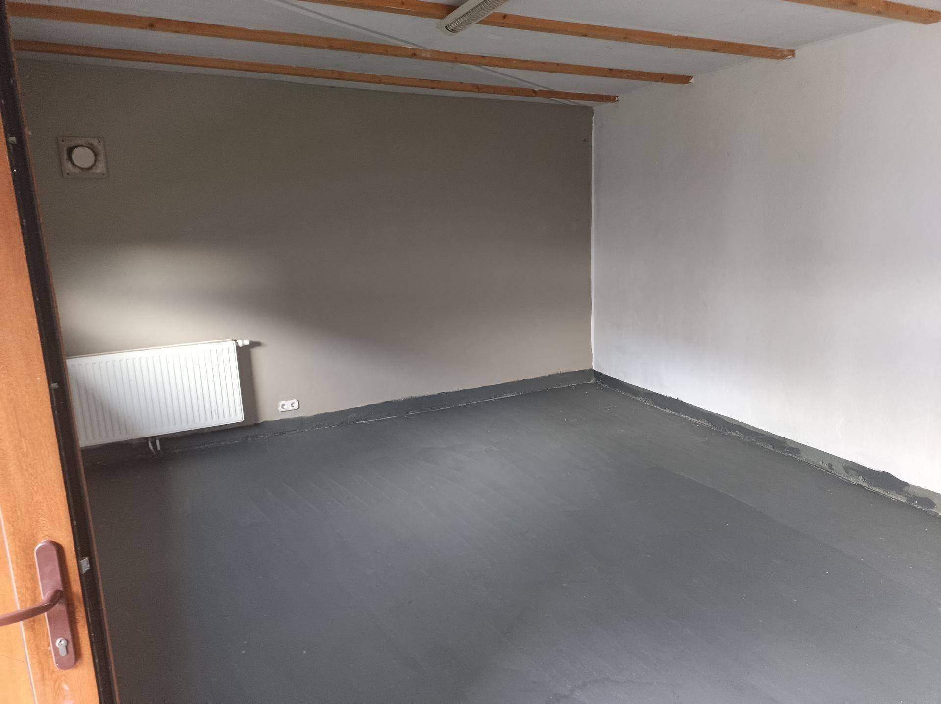 Leerer Raum mit grau gestrichenen Wänden, Heizkörper und einfacher Deckenkonstruktion.