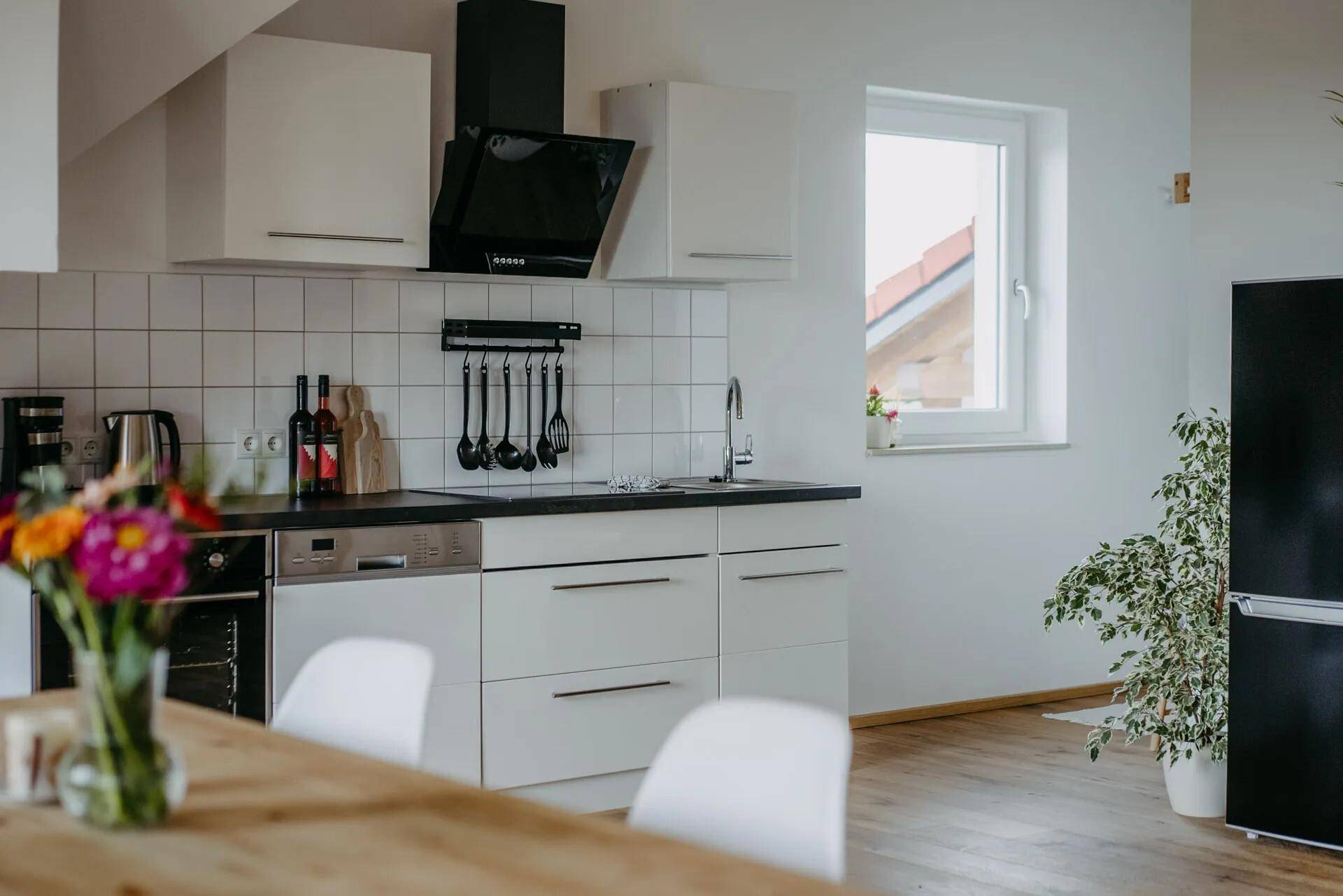 Moderne Küche mit weißen Schränken, integrierten Geräten und Fensterblick ins Grüne.