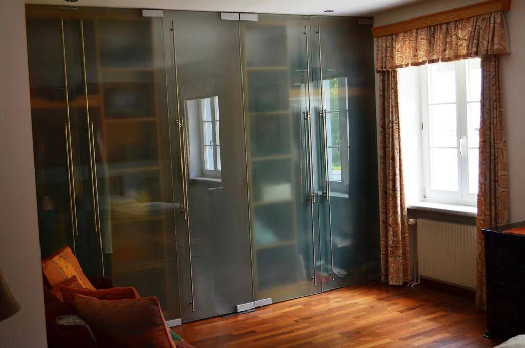 Schlafzimmer mit großem Kleiderschrank aus Milchglas und Fenster mit Vorhängen.