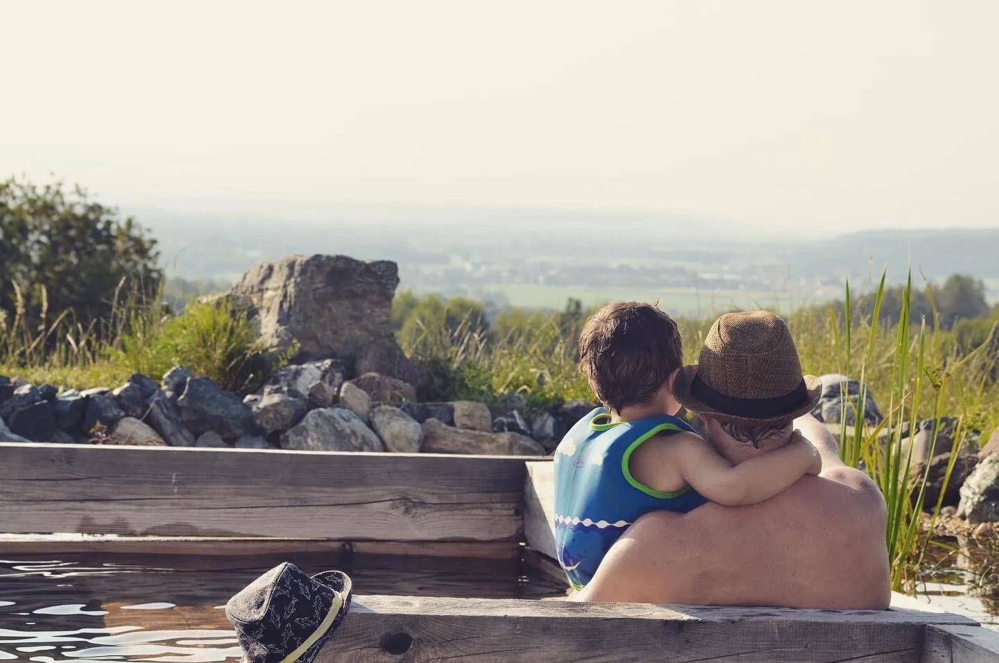 Zwei Personen genießen den Ausblick aus einem hölzernen Whirlpool in der Natur.