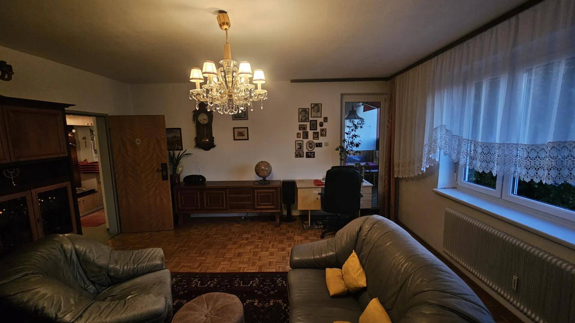 Klassisch eingerichtetes Wohnzimmer mit Parkettboden und Kronleuchter in gedämpftem Licht.