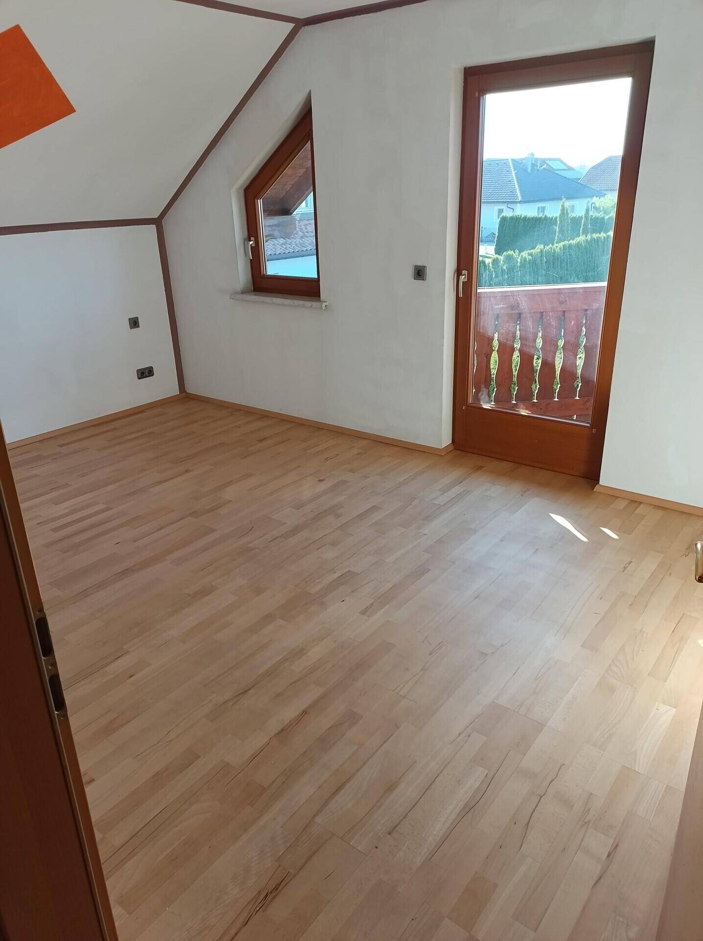 Helles Schlafzimmer mit Holzboden und Zugang zu einem kleinen Balkon.