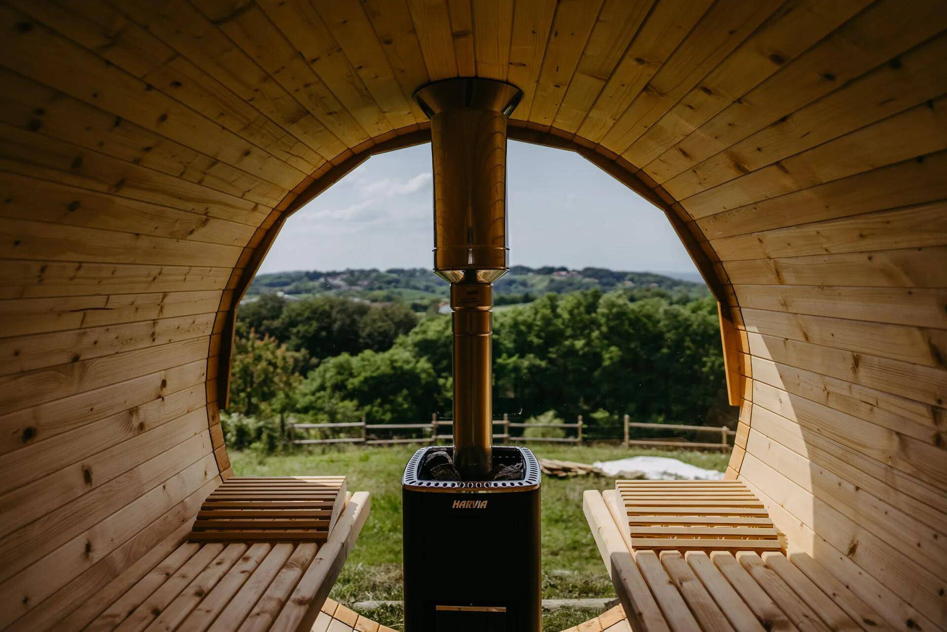 Gemütliche Fasssauna aus Holz mit Blick auf die grüne Landschaft.