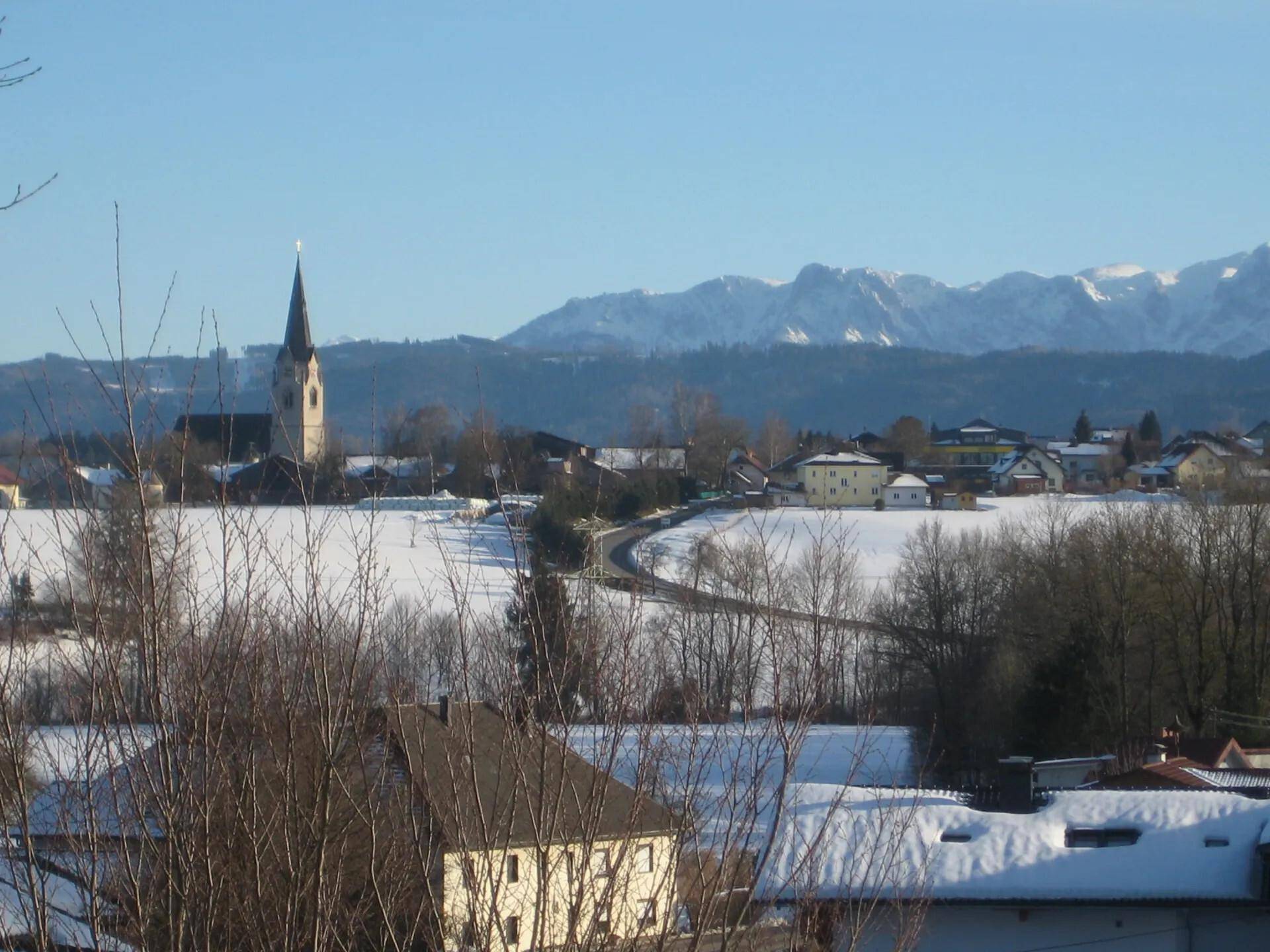 Winterlicher Panoramablick auf ein verschneites Dorf mit Kirche und majestätischen Bergen.