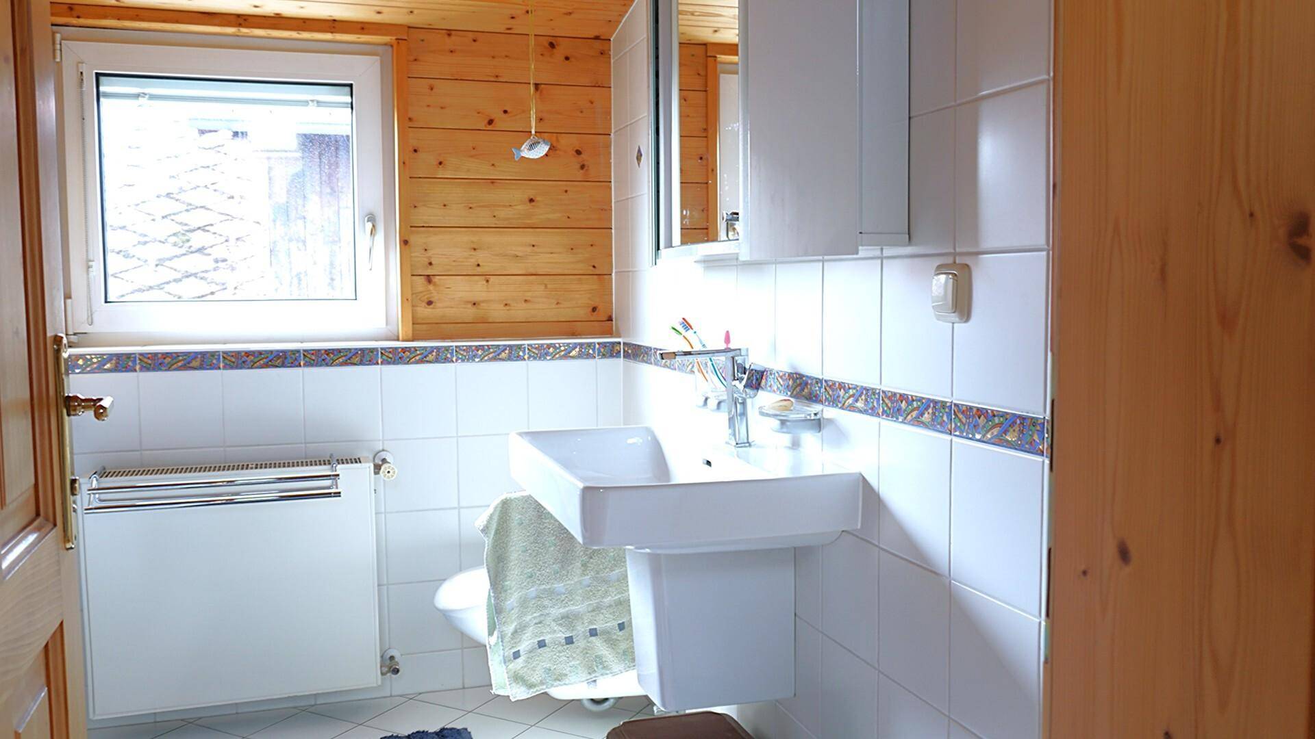 Badezimmer mit Waschbecken, Spiegelschrank und holzverkleideten Wänden.