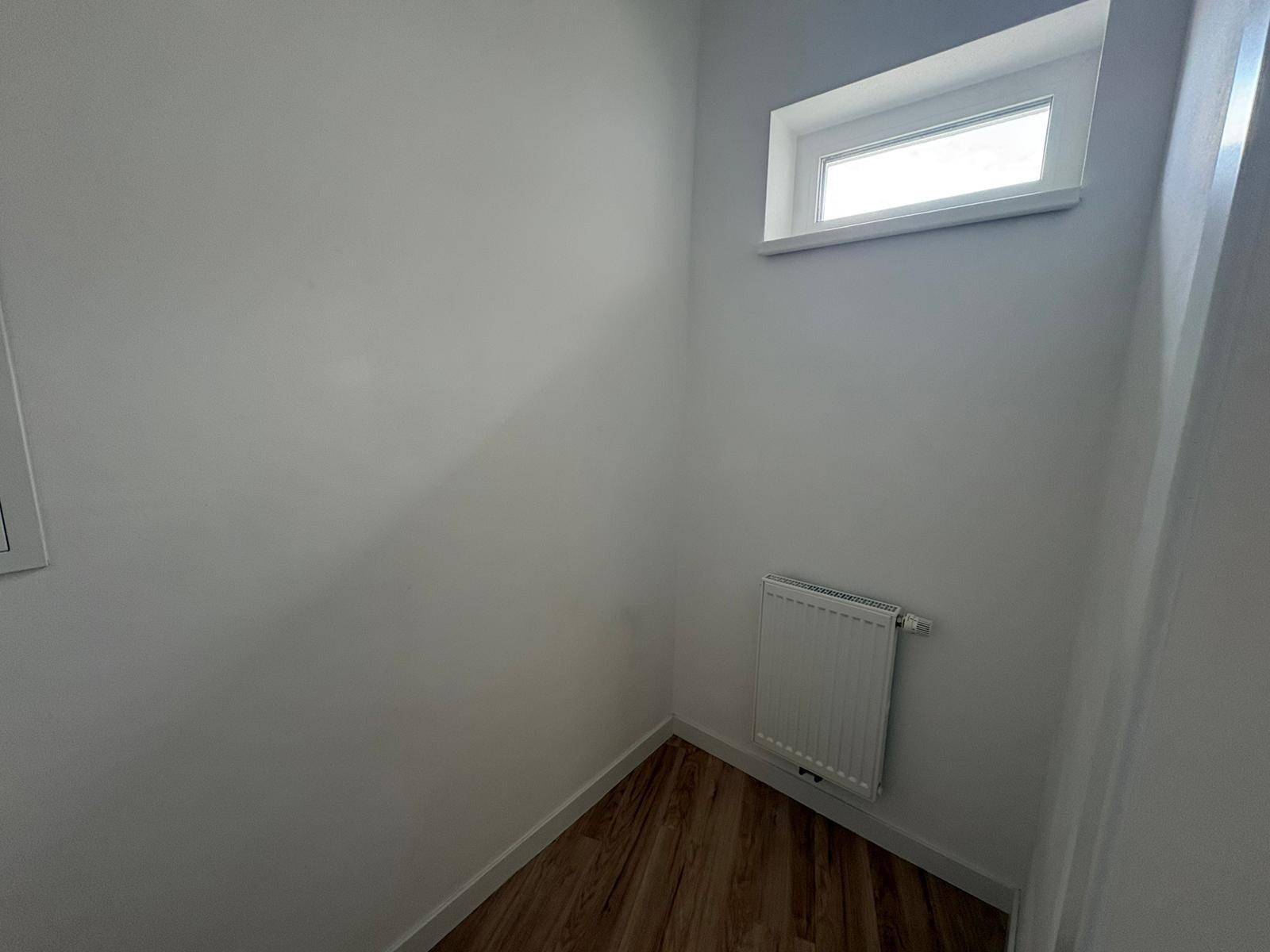 Kleiner Nischenbereich mit Heizkörper und Fenster, ausgestattet mit hellem Laminatboden.