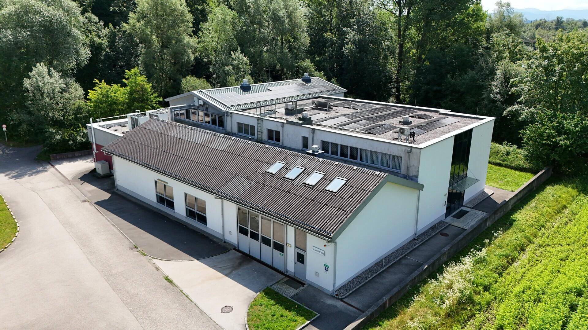 Luftaufnahme eines modernen Industriegebäudes mit Flachdach und umliegender grüner Landschaft.