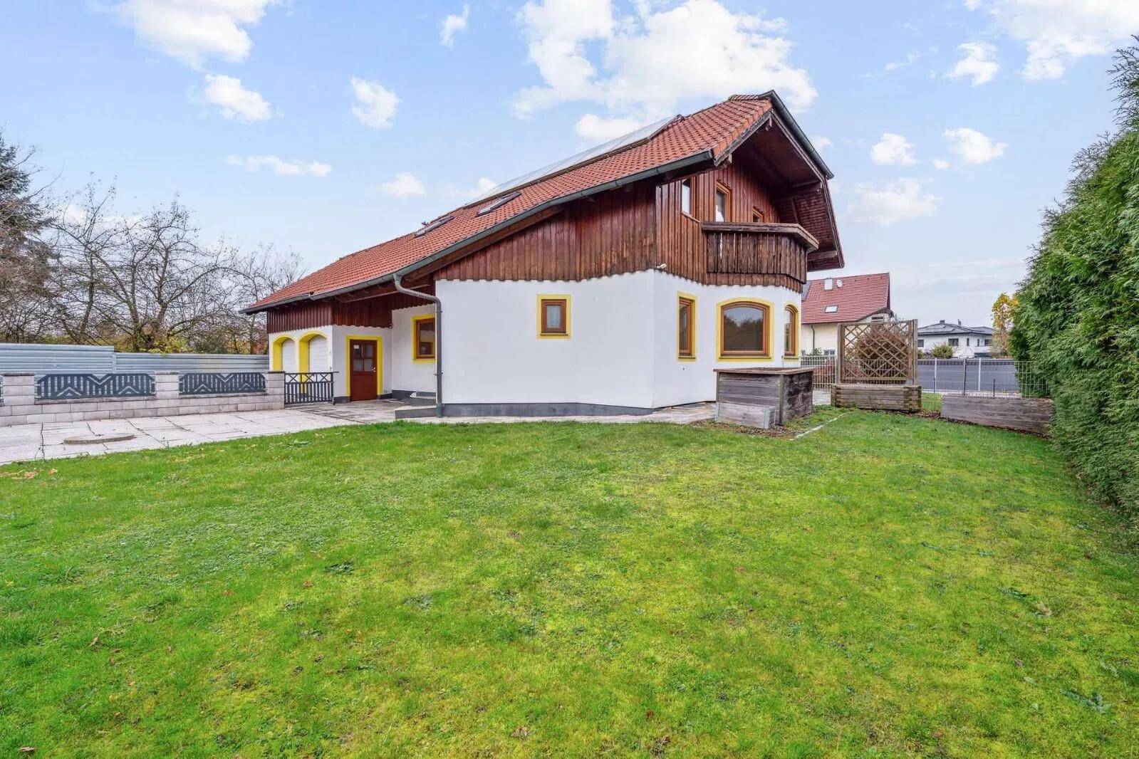 Seitenansicht des Hauses mit großem Rasenbereich und Holzbalkon im Obergeschoss.