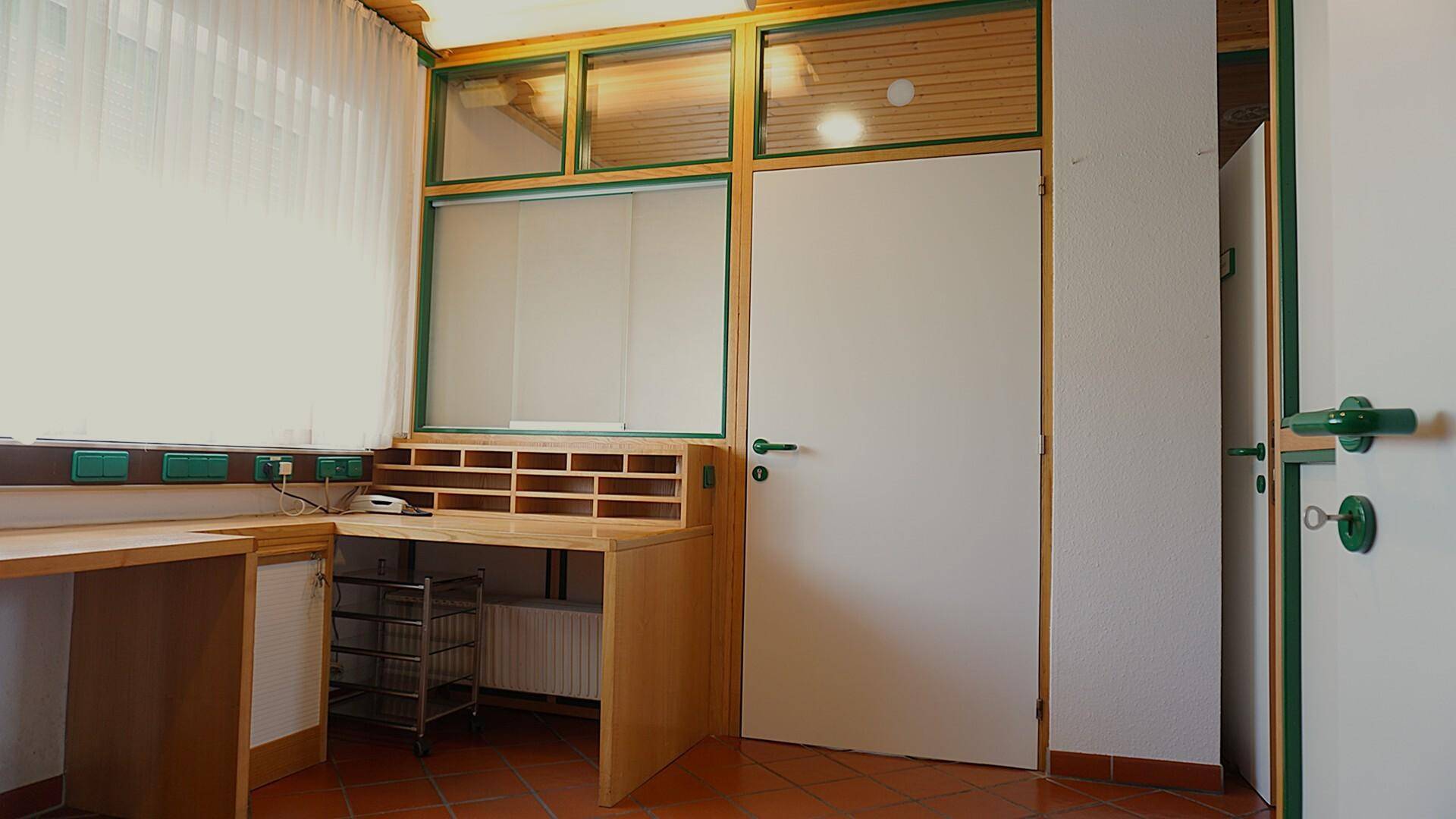 Büroraum mit Holzschreibtisch, Regalen und Fenster mit Jalousien.