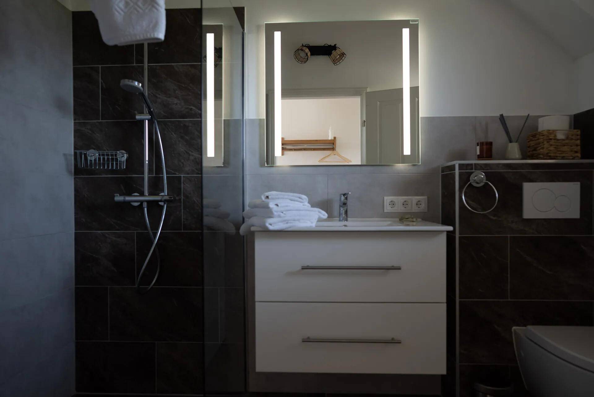 Modernes Badezimmer mit Dusche, Waschtisch und beleuchtetem Spiegel.