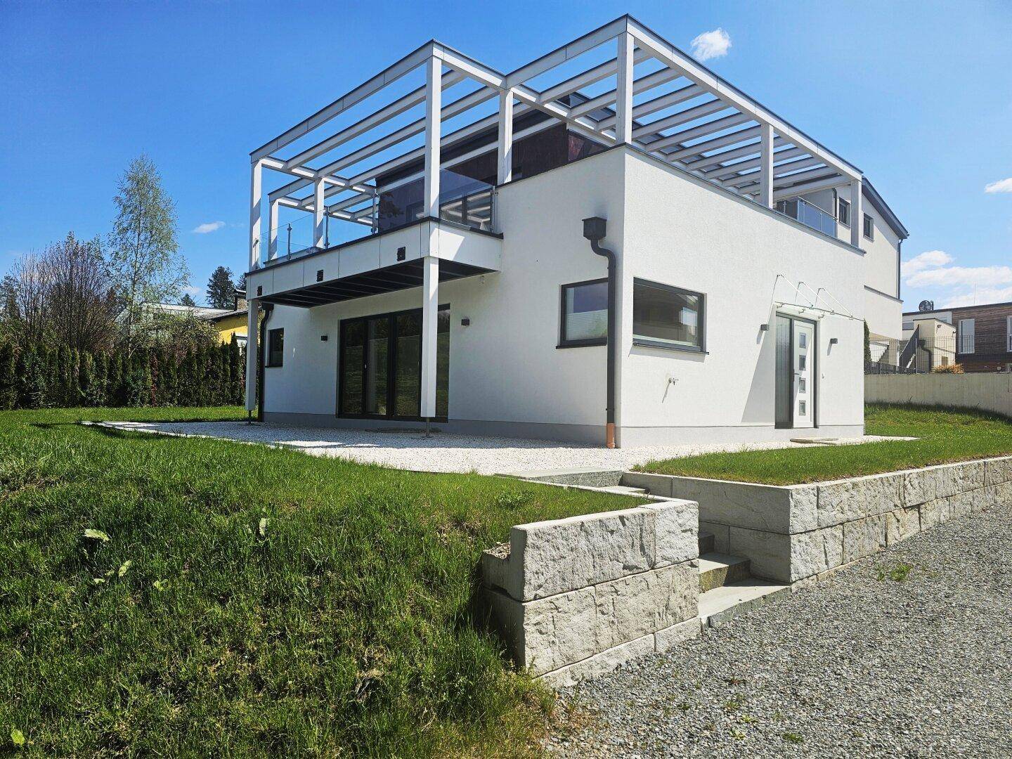 Modernes Einfamilienhaus mit weißer Fassade, Flachdach und großzügiger Dachterrasse.