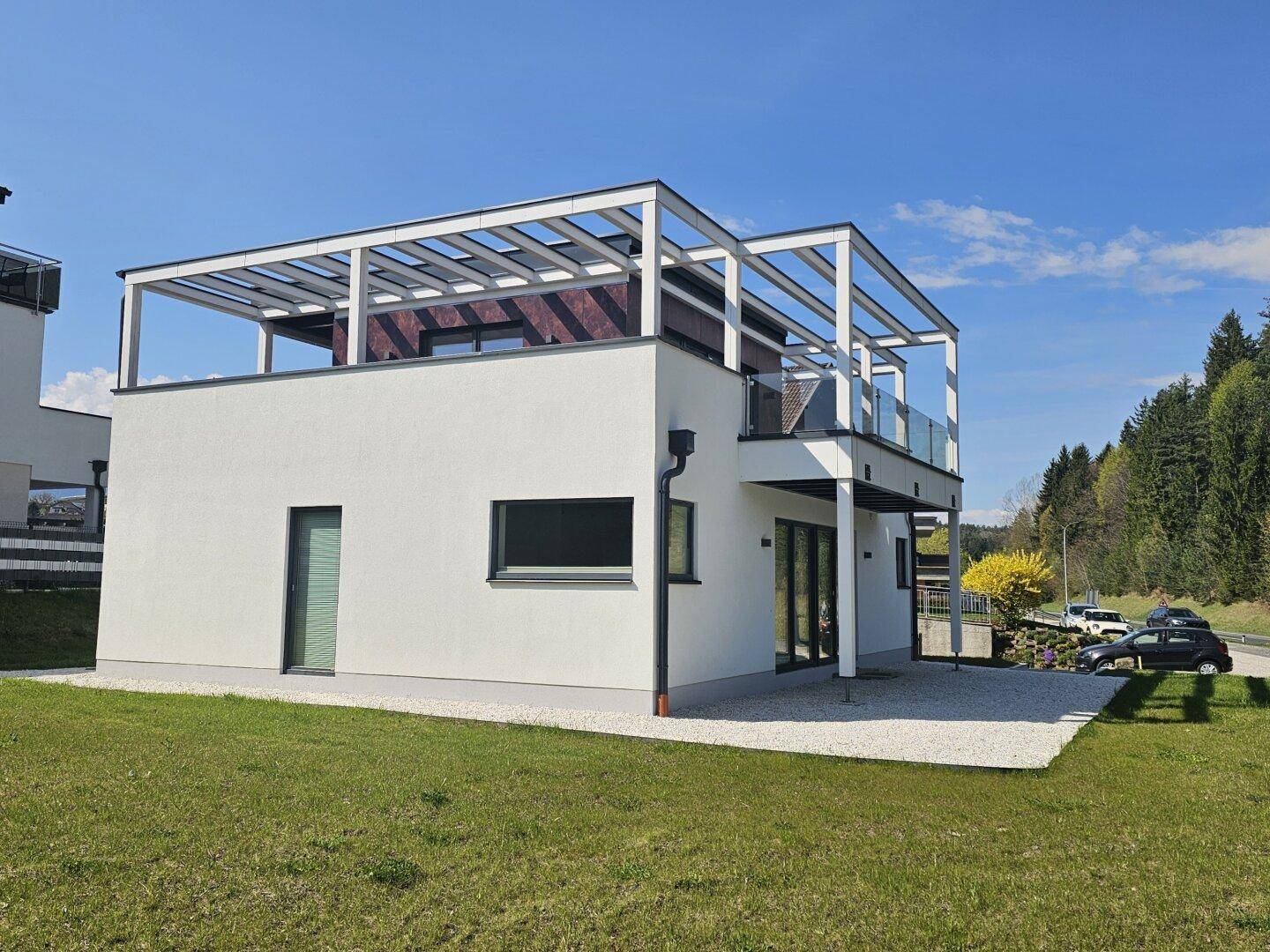 Ansicht des modernen Hauses von der Seite mit weißer Fassade und umliegender Grünfläche.