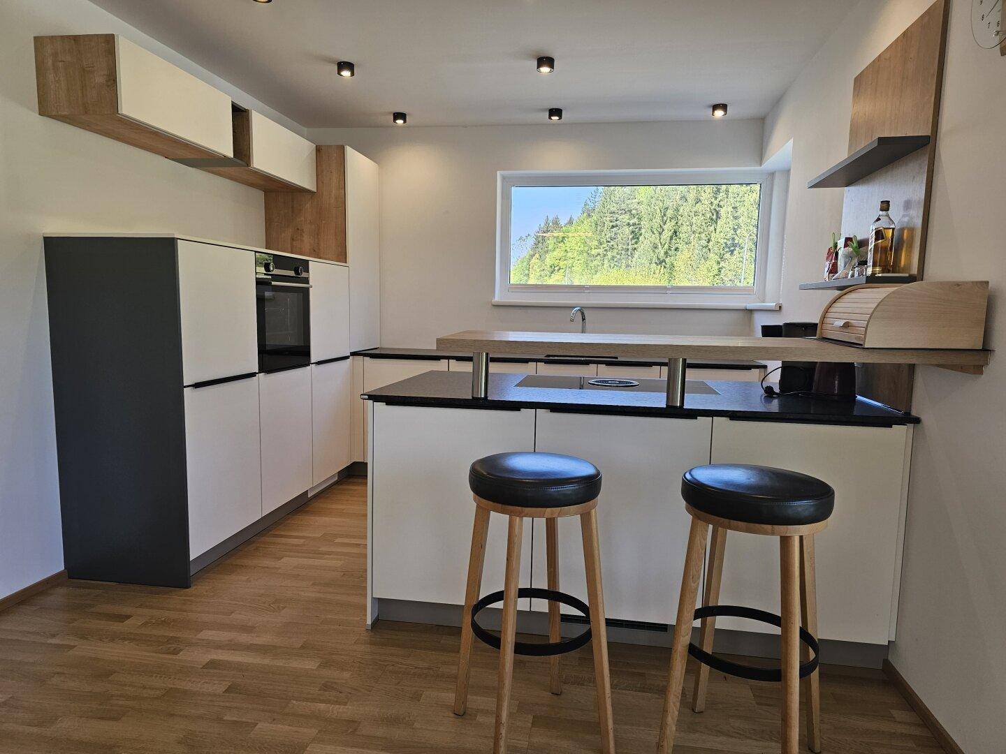 Moderne Küche mit Kochinsel, integrierten Geräten und Blick ins Grüne durch das Fenster.
