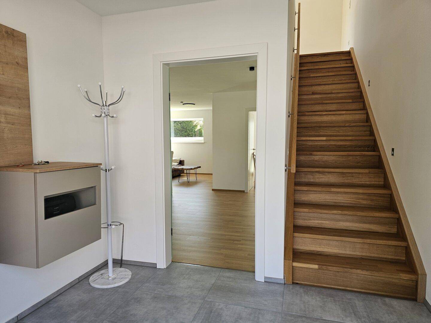 Heller Eingangsbereich mit Holztreppe und Garderobe, der in den Wohnbereich führt.