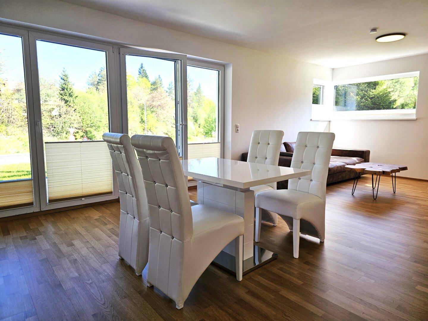 Lichtdurchfluteter Wohn-Essbereich mit großen Fenstern, Holzboden und Zugang zur Terrasse.