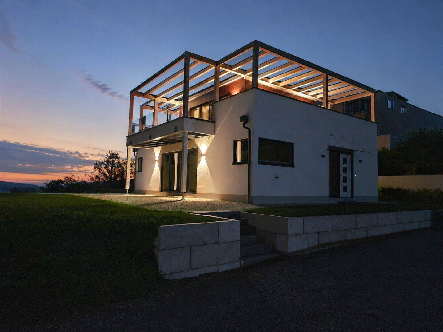 Frontansicht des modernen Hauses bei Dämmerung mit beleuchtetem Eingangsbereich und Treppe.