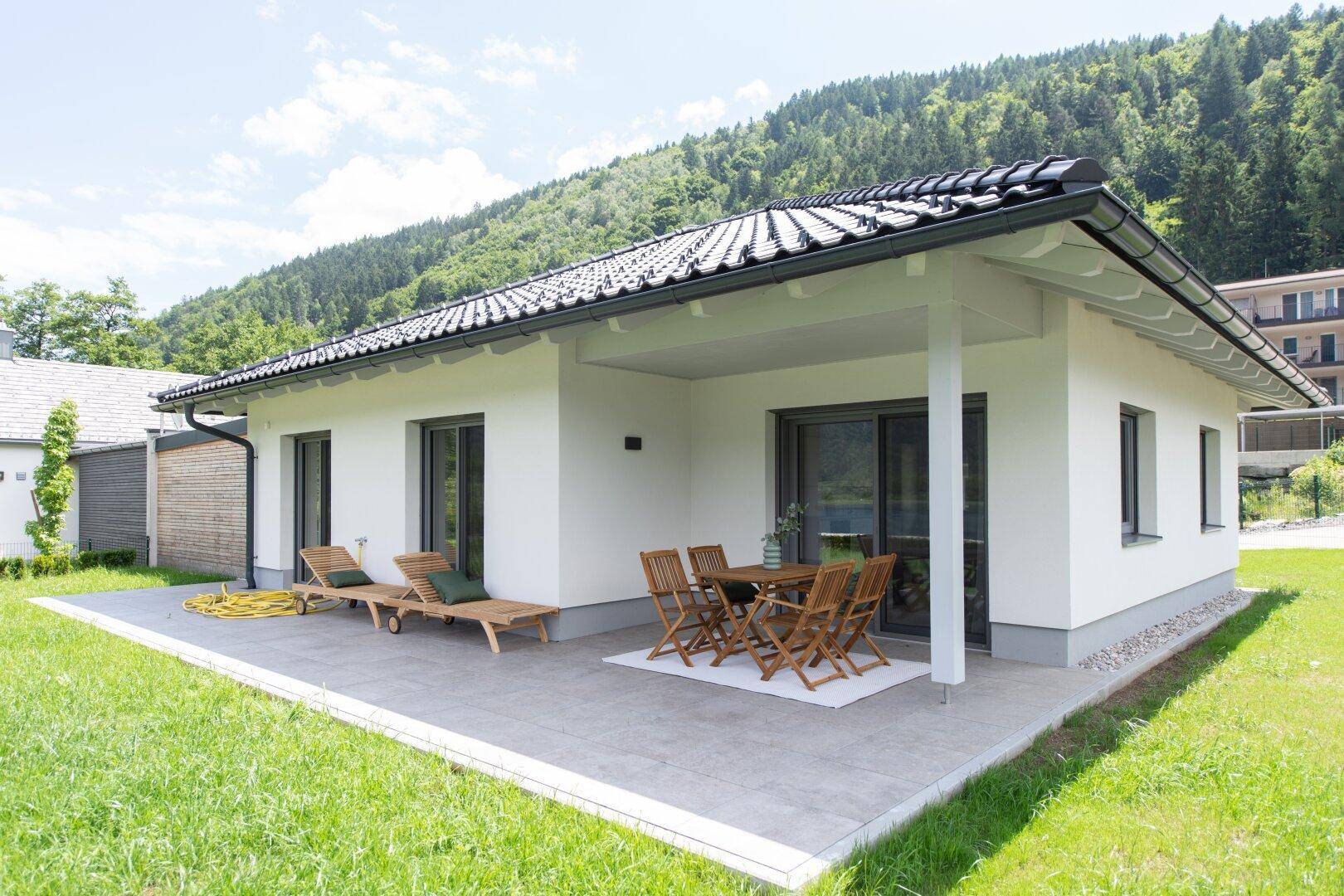 Modernes Einfamilienhaus mit großer Terrasse, Gartenmöbeln und Bergblick.