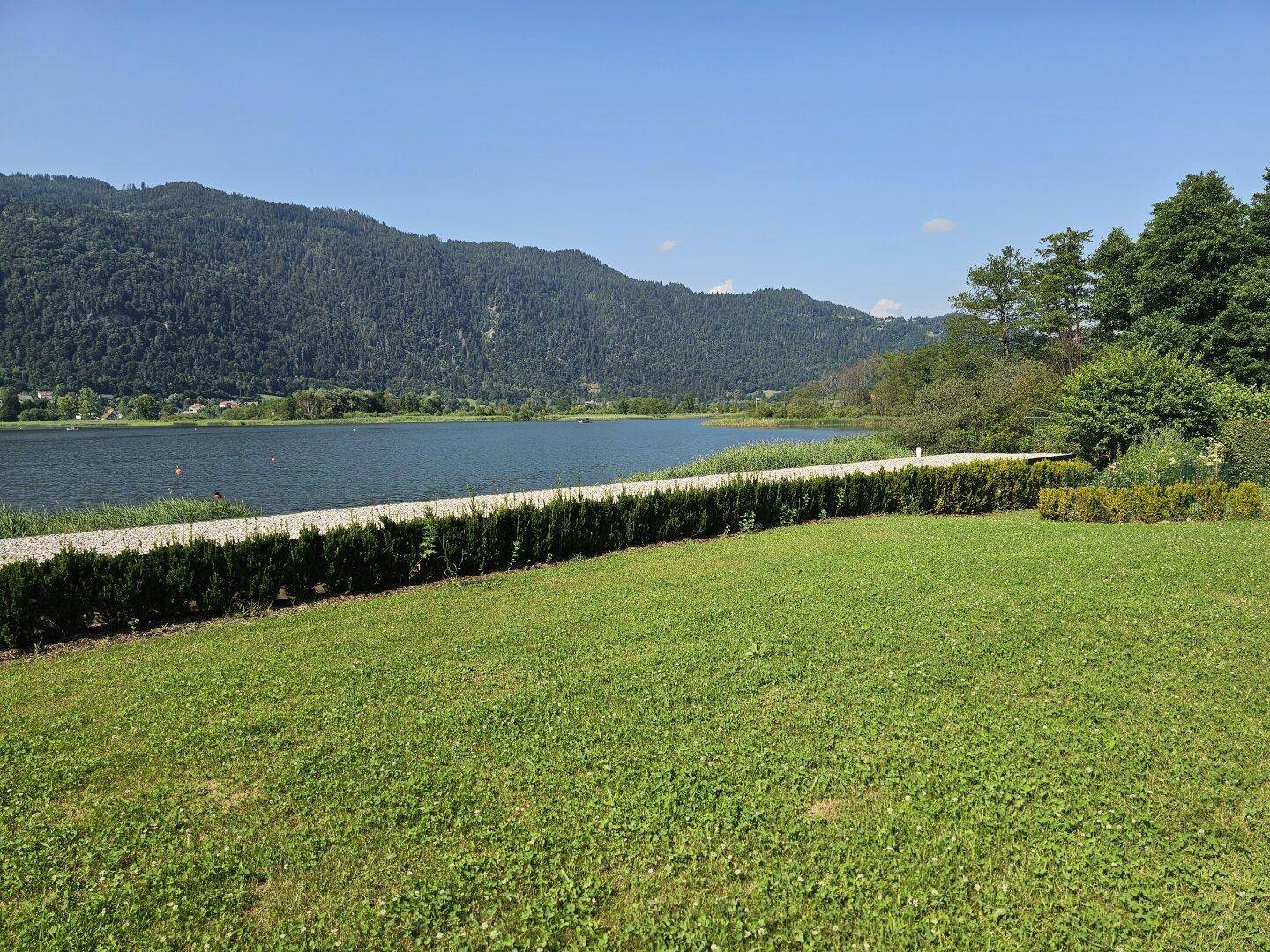 Gepflegte Rasenfläche mit Hecke und Blick auf den See und die umliegenden Berge.