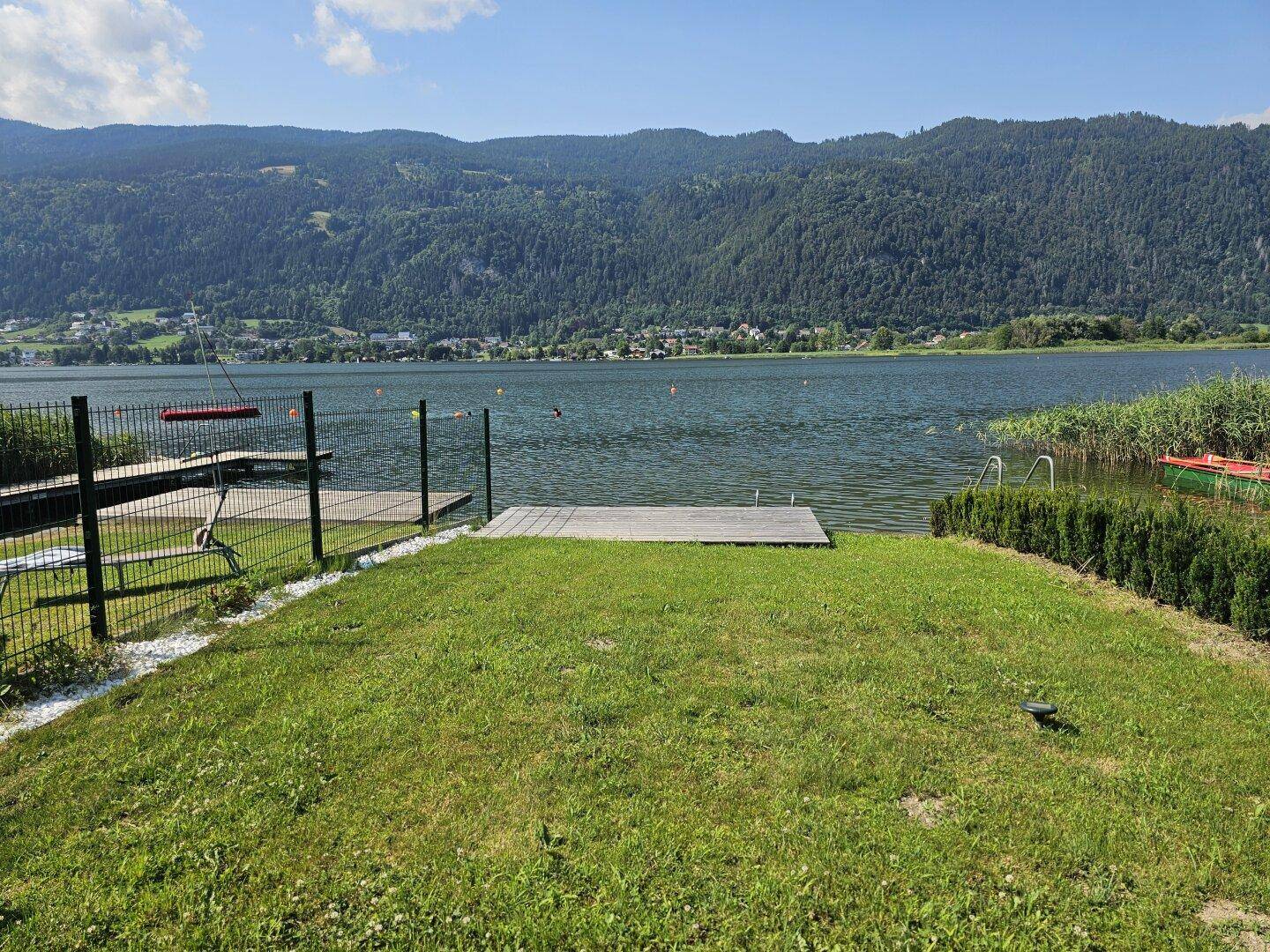 Gartenbereich mit Rasen und direktem Zugang zum See über einen kleinen Steg.