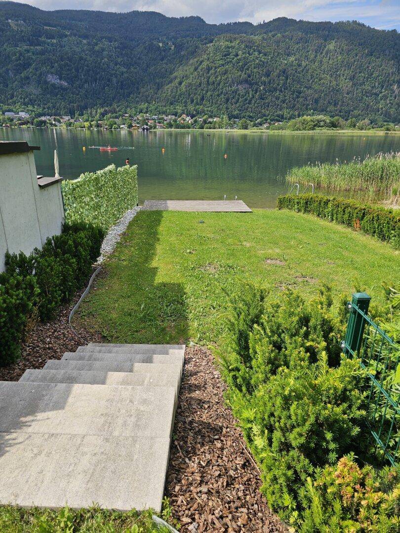 Gepflegter Gartenbereich mit Steintreppe, die zu einem privaten Seezugang mit Holzsteg führt.