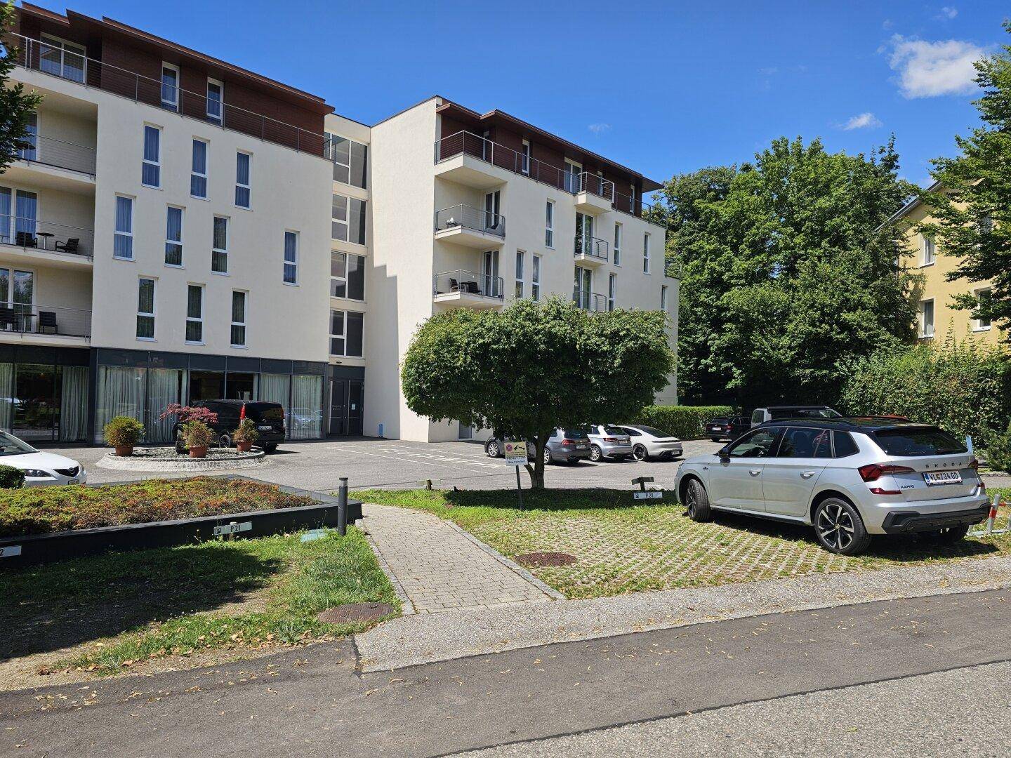 Modernes Apartmentgebäude mit mehreren Etagen, Balkonen und Parkplätzen im Freien.