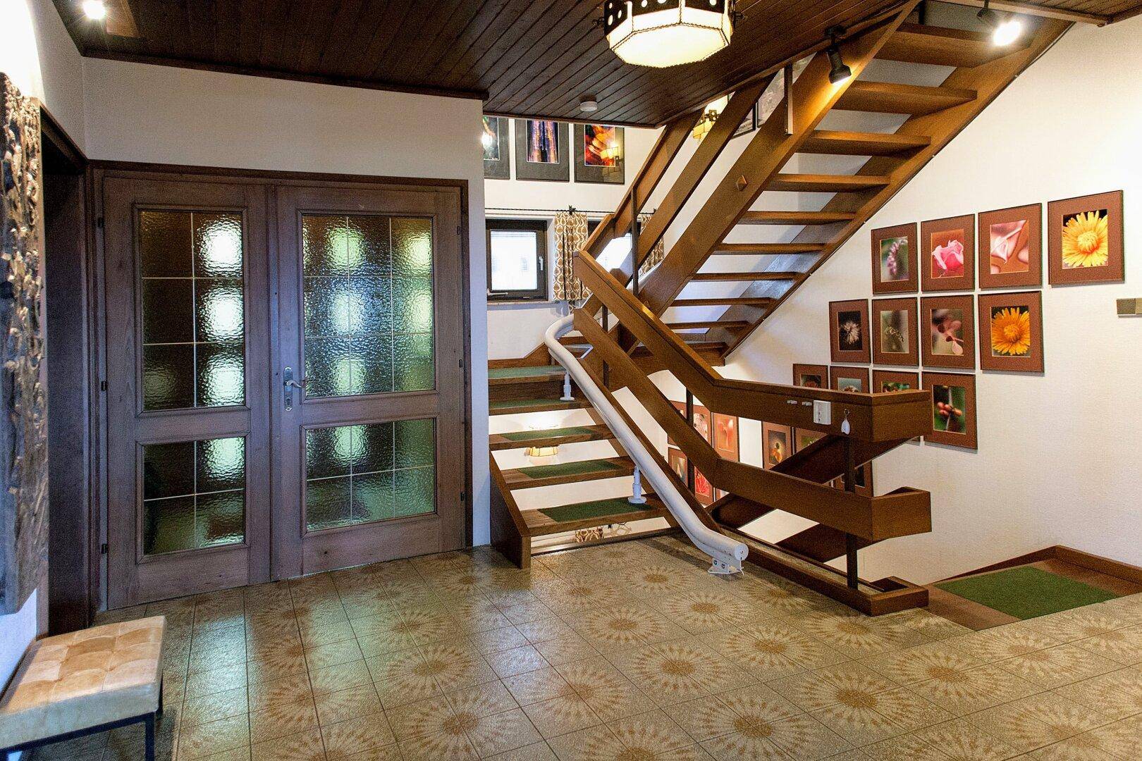 Geräumiger Flur mit Holztreppe, gemusterten Fliesen und einer Galerie von Bildern an der Wand.