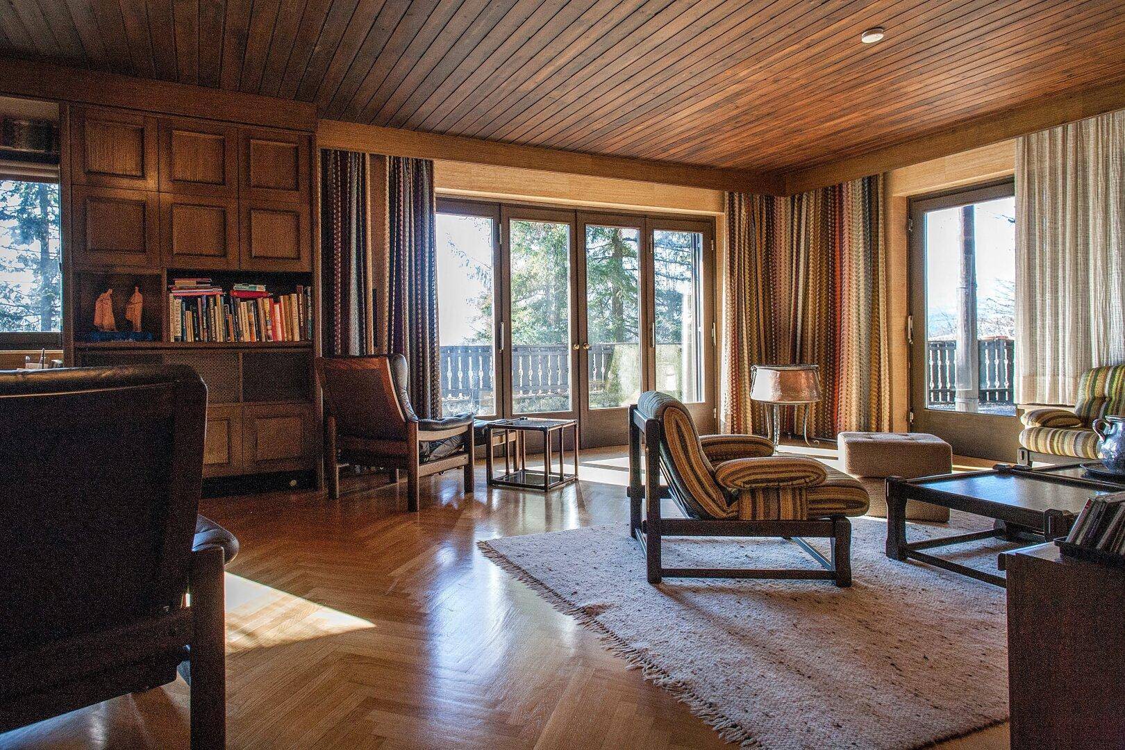Gemütliches Wohnzimmer mit Holzparkett, Holzbalkendecke und Zugang zu einem Balkon mit Weitblick.