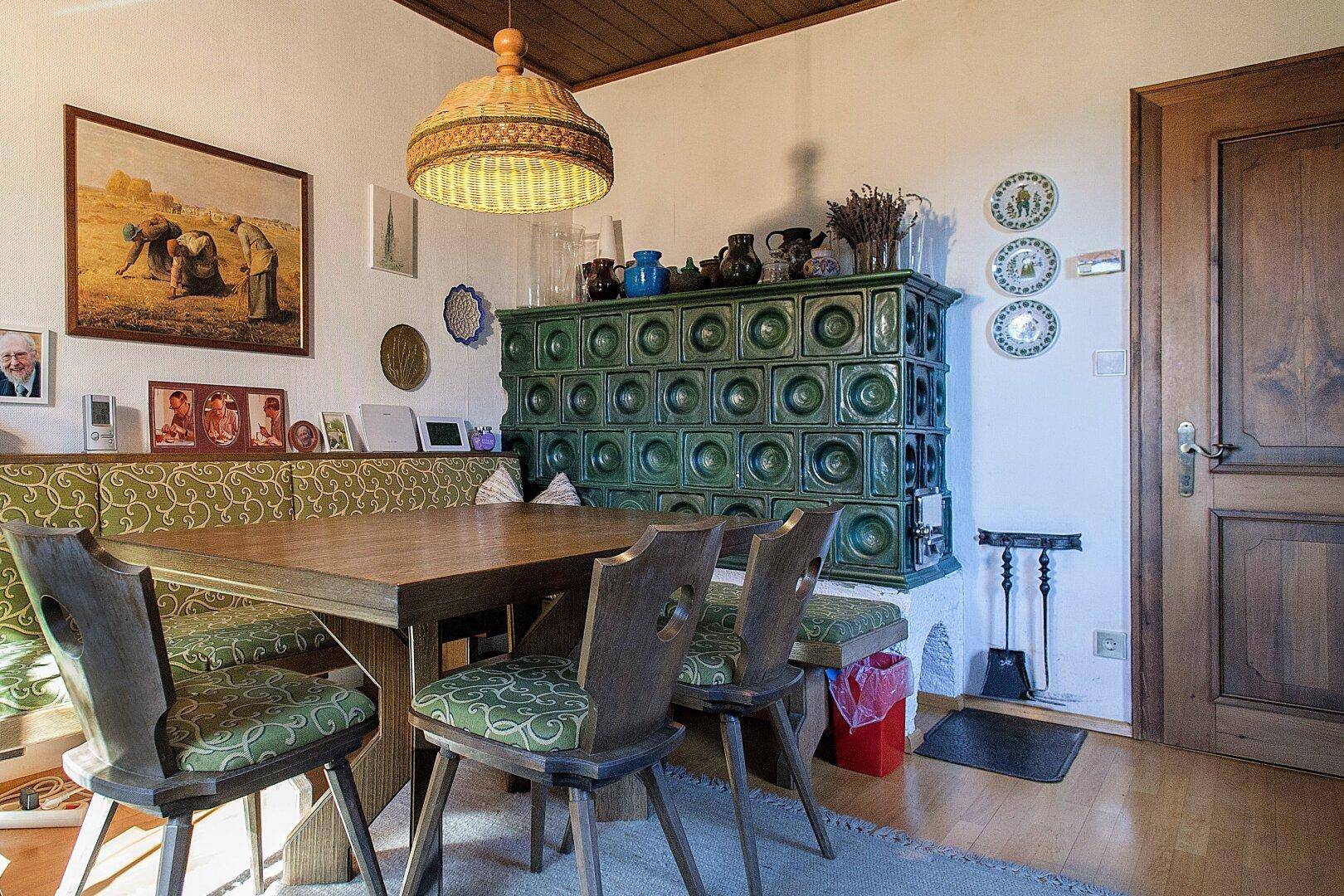 Traditioneller Essbereich mit grünem Kachelofen, Holztisch und gemütlicher Eckbank.