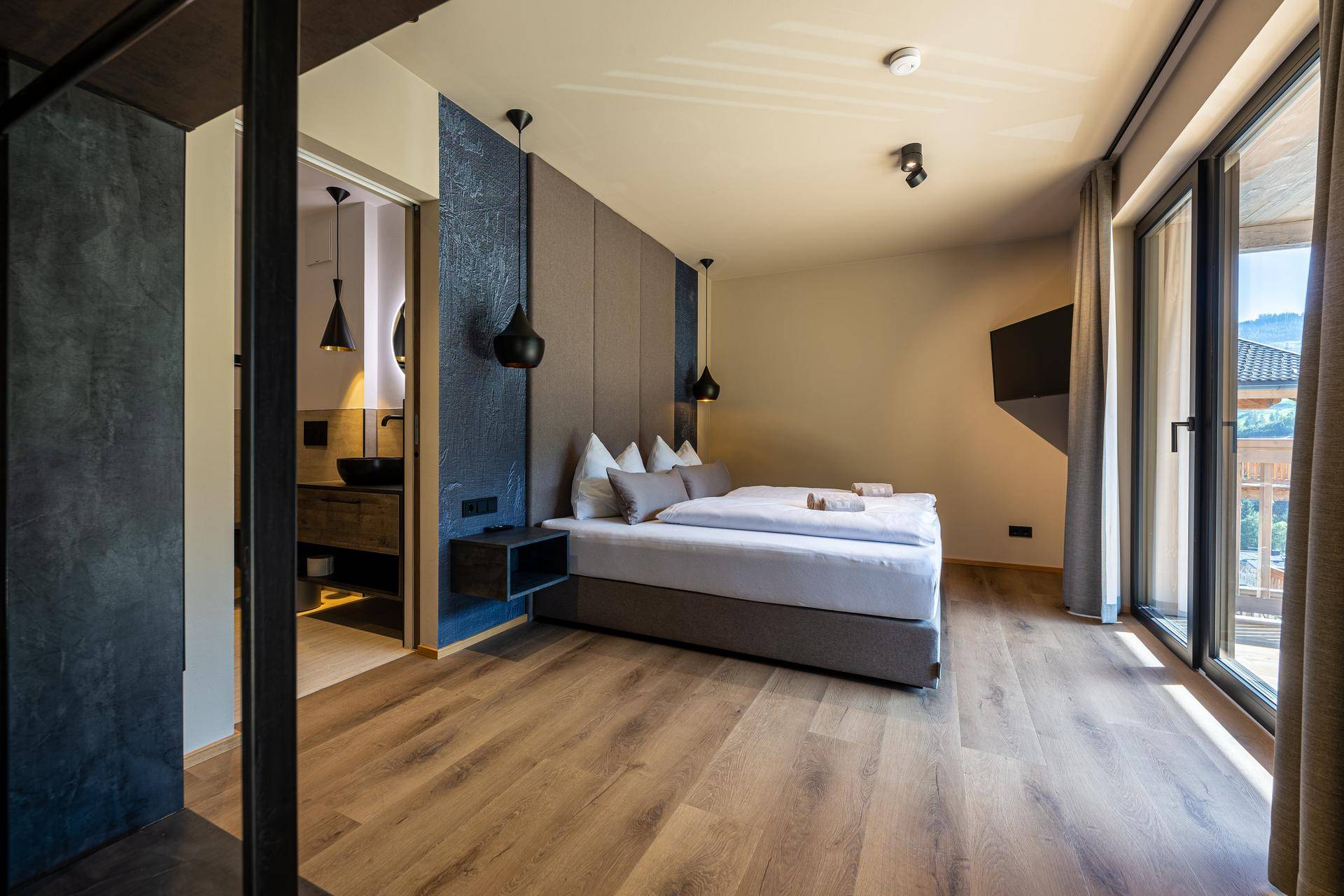 Helles Schlafzimmer mit Holzboden, großem Fenster und direktem Zugang zum Badezimmer.