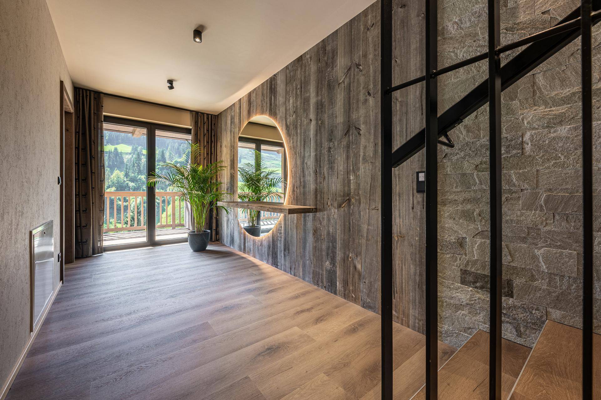 Heller Flur mit Holzwand, Steinakzenten und Zugang zu einem Balkon mit Bergblick.