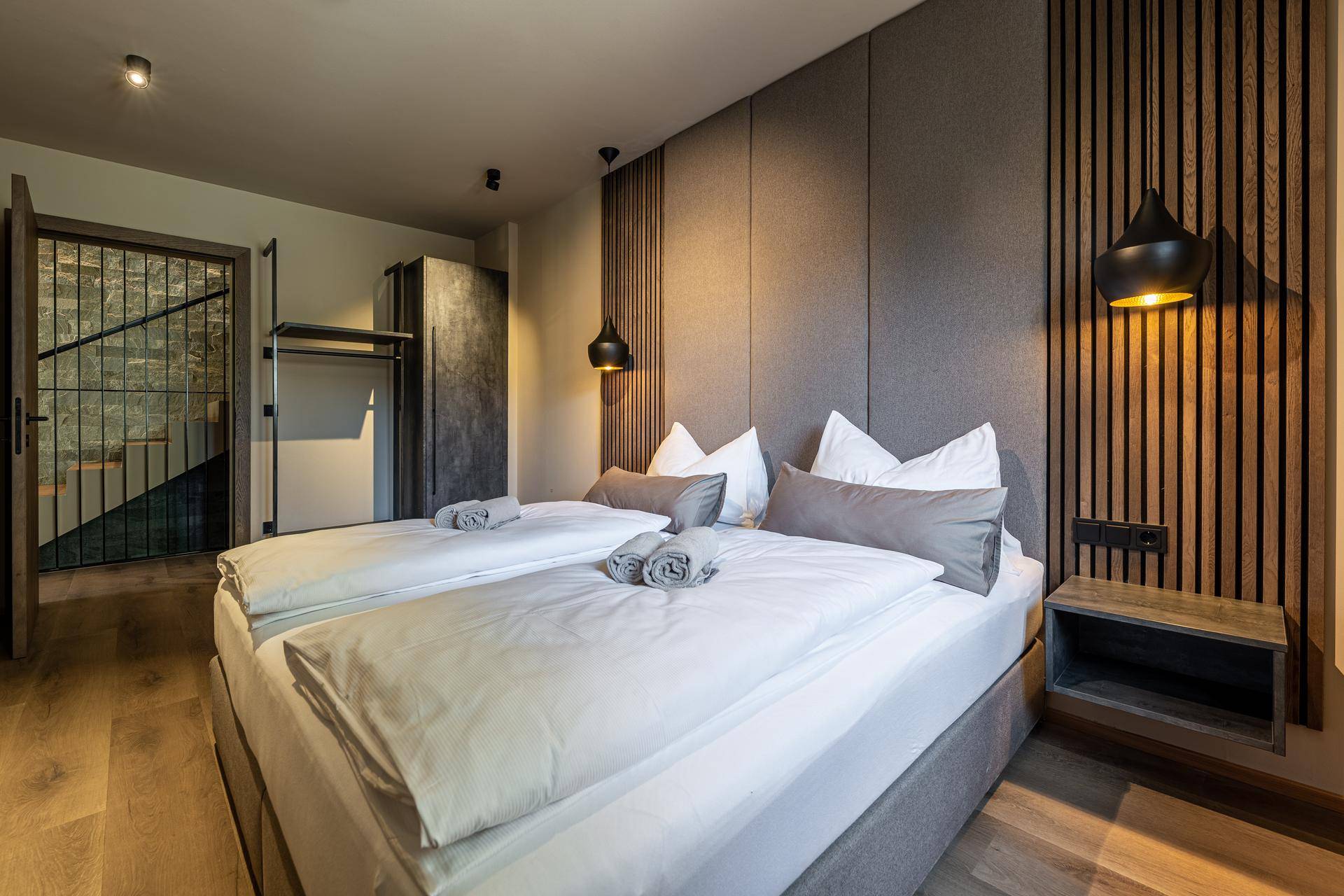 Modernes Schlafzimmer mit Doppelbett, Holzboden und stilvoller Wandverkleidung.