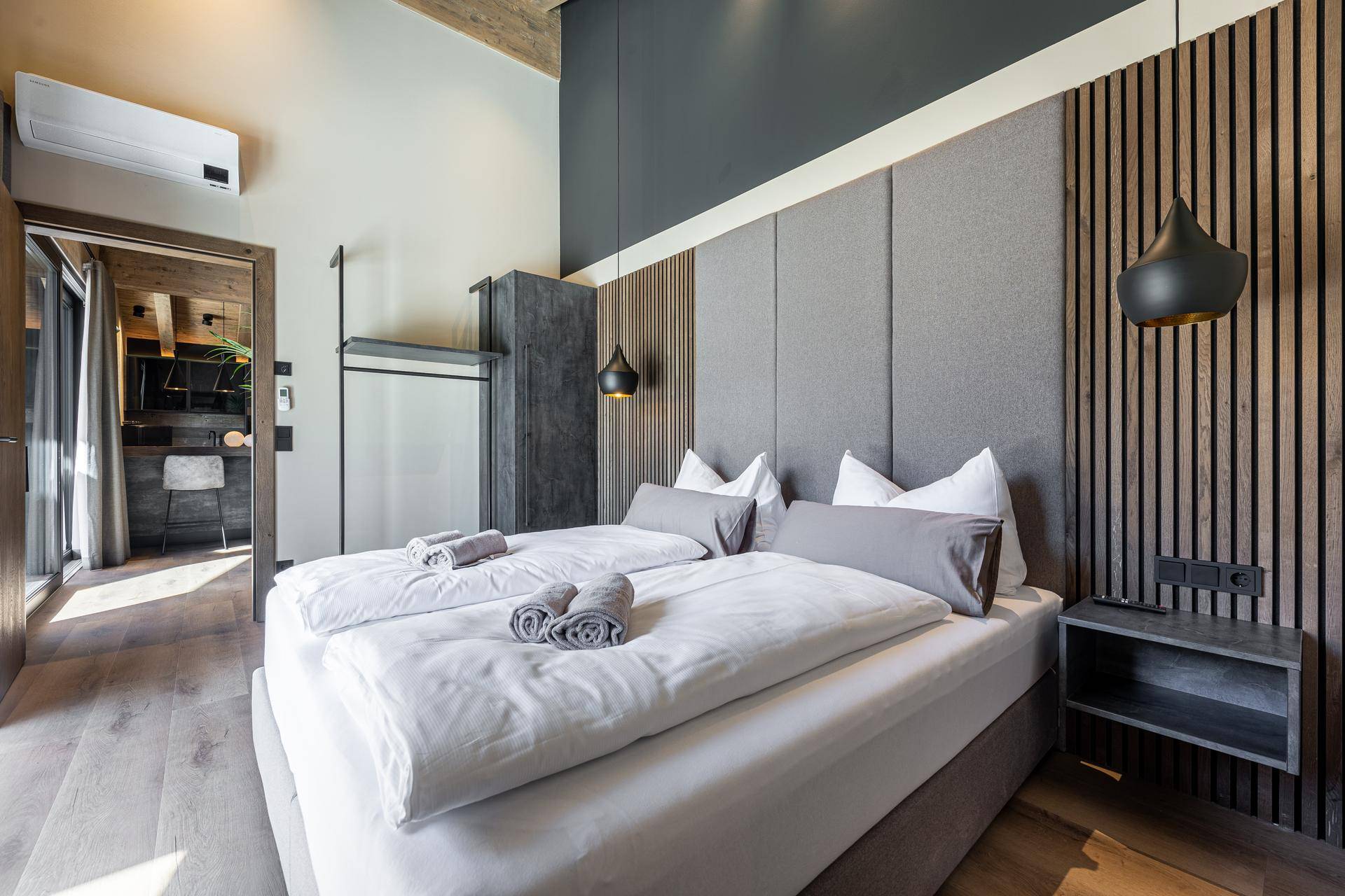 Helles Schlafzimmer mit Holzboden, gepolstertem Kopfteil und Zugang zu einem weiteren Raum.