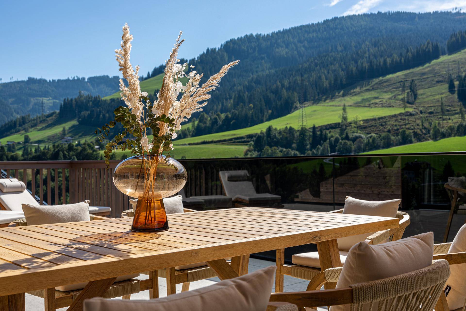 Sonnige Terrasse mit Esstisch und Dekoration, umgeben von einer malerischen Berglandschaft.