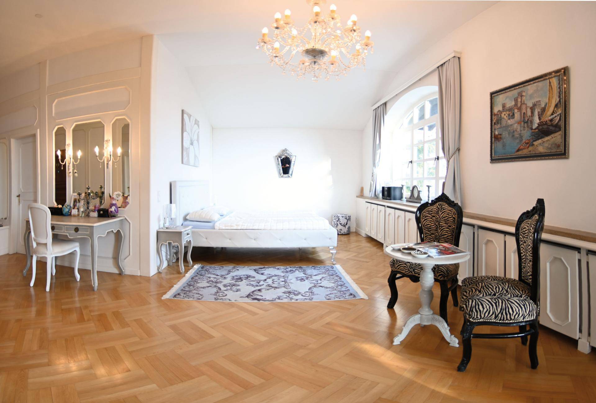 Helles Schlafzimmer mit Fischgrätparkett, Kronleuchter und elegantem Schminktisch.