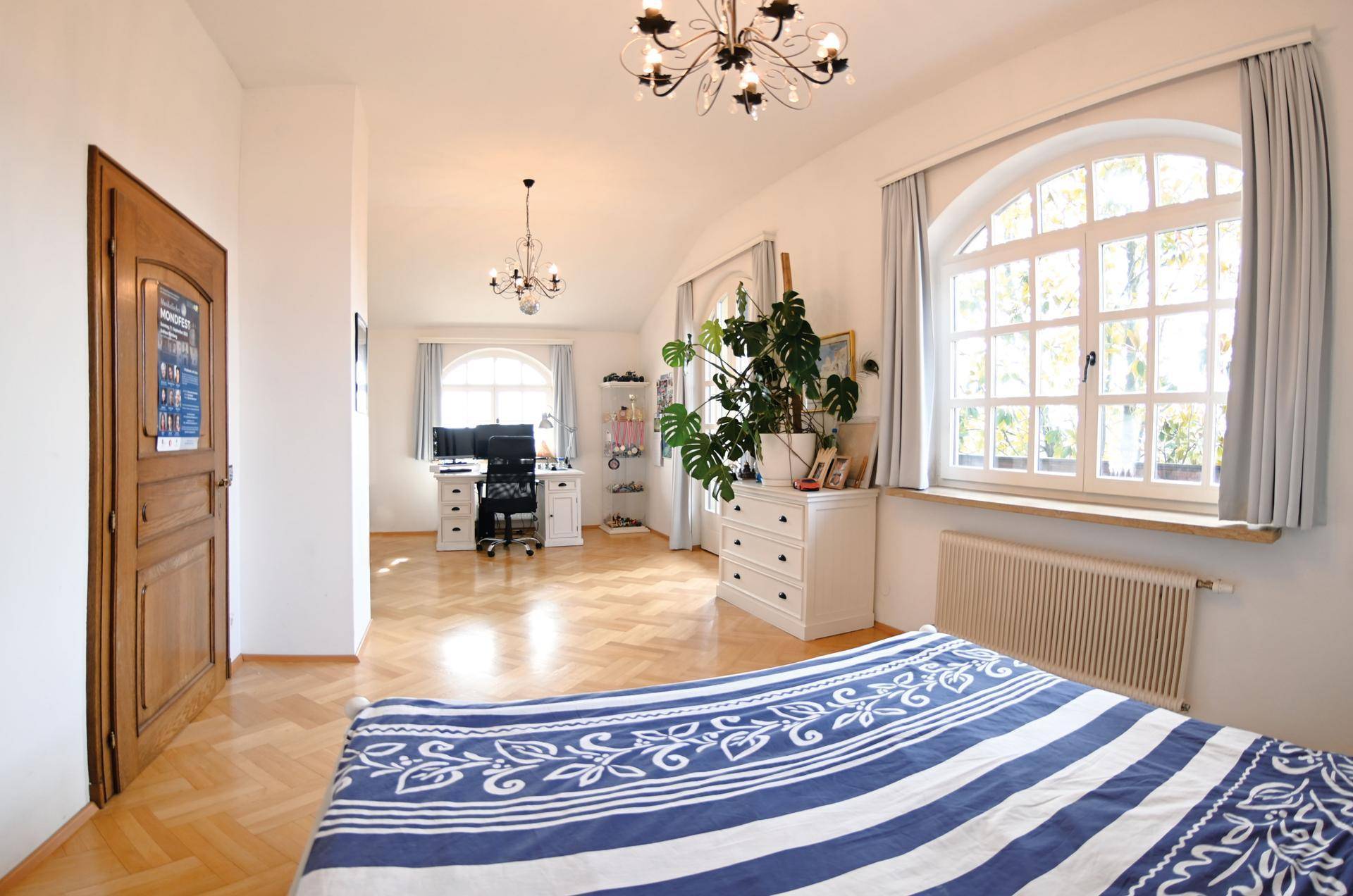 Helles Schlafzimmer mit integriertem Arbeitsbereich, Parkettboden und großen Fenstern.