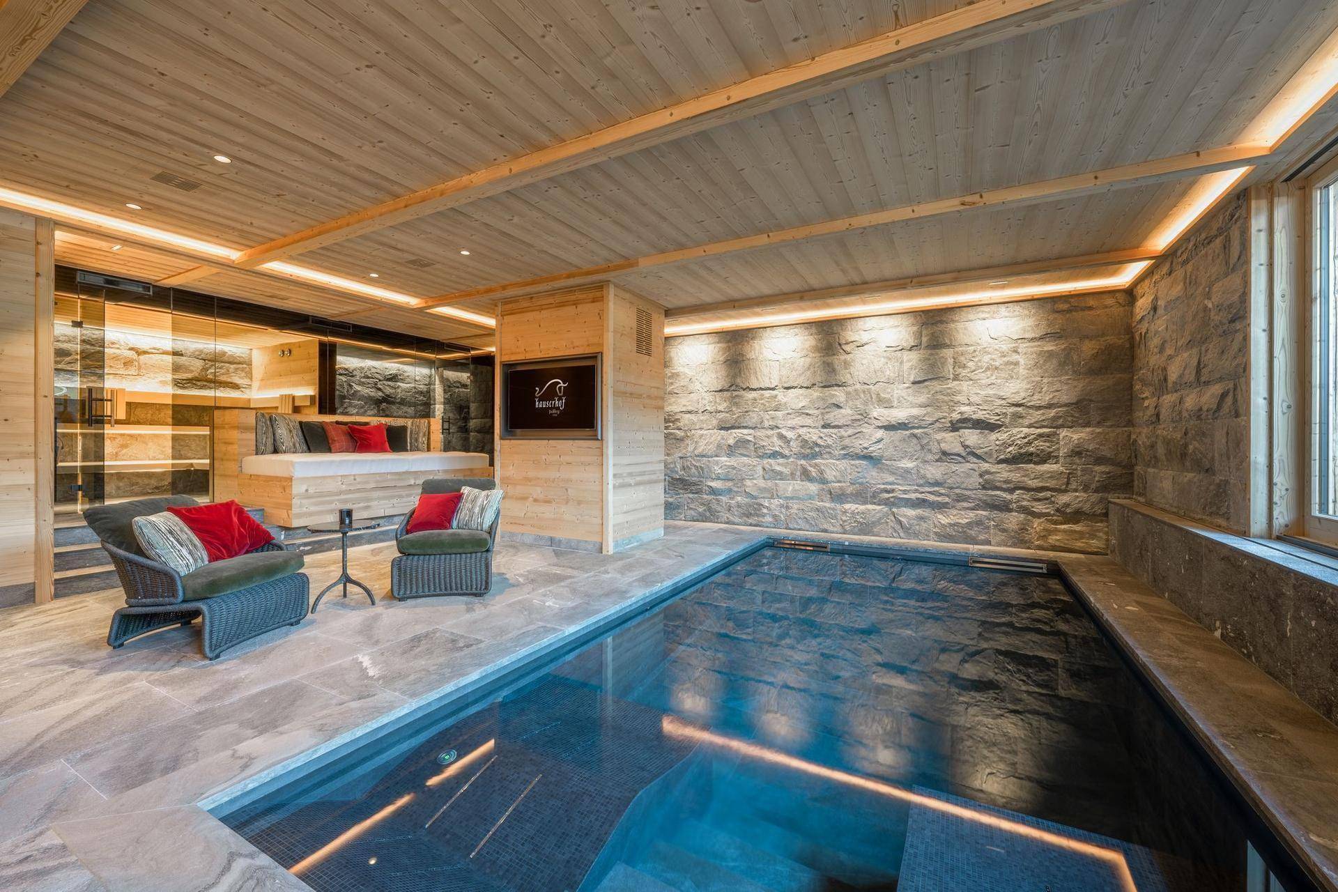 Luxuriöser Innenpoolbereich mit Steinwand, Entspannungsliegen und stimmungsvoller Beleuchtung.