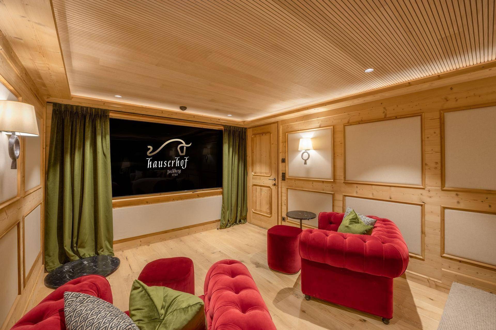 Exklusiver Medienraum mit großer Projektionsfläche, bequemen roten Sofas und Holzvertäfelung.