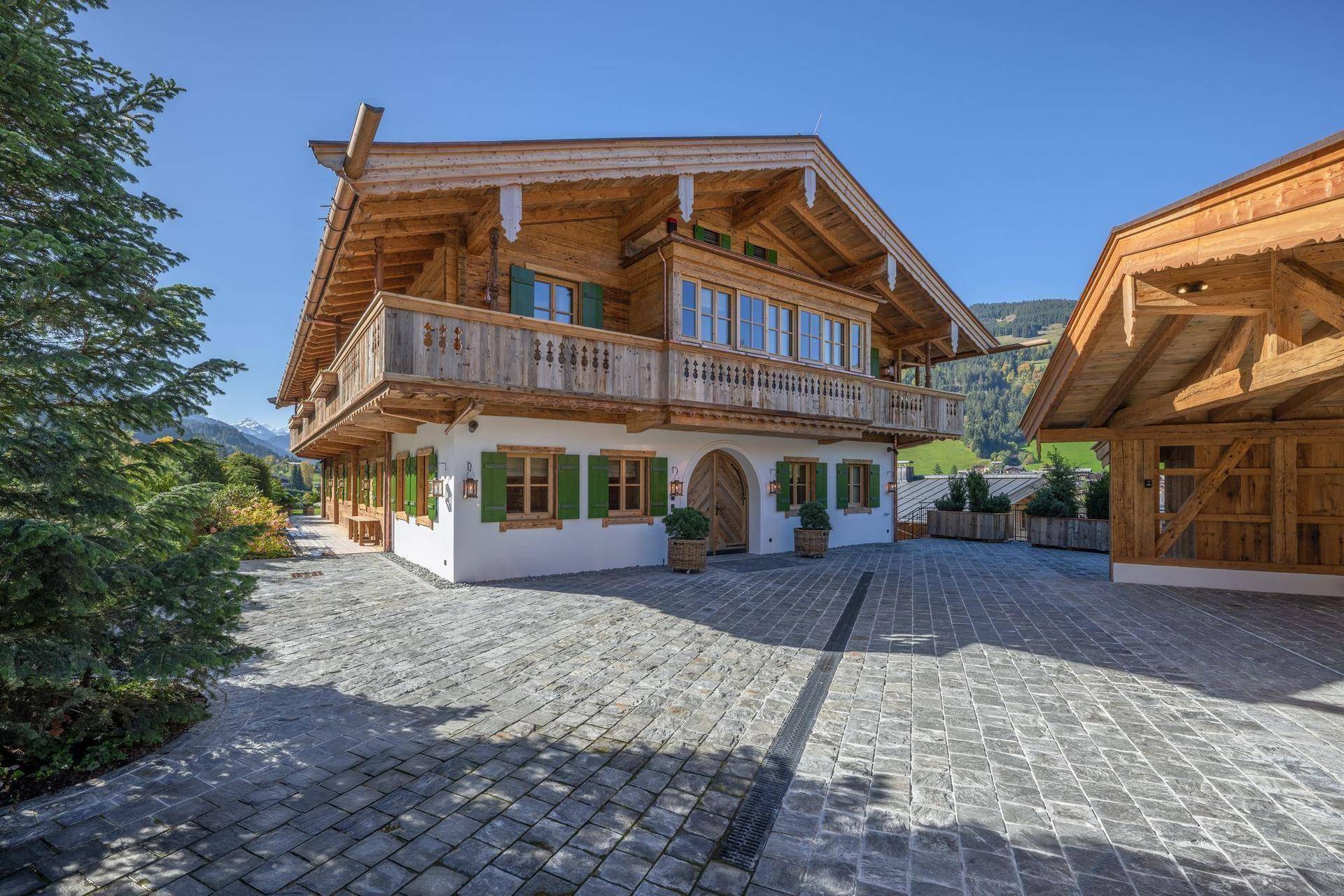 Eindrucksvolles Holzchalet mit weißer Fassade, grünen Fensterläden und gepflasterter Zufahrt.