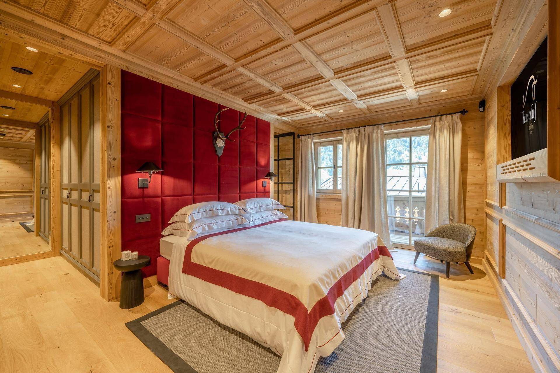Gemütliches Schlafzimmer mit Holztäfelung, rotem Kopfteil und Zugang zu einem Balkon.