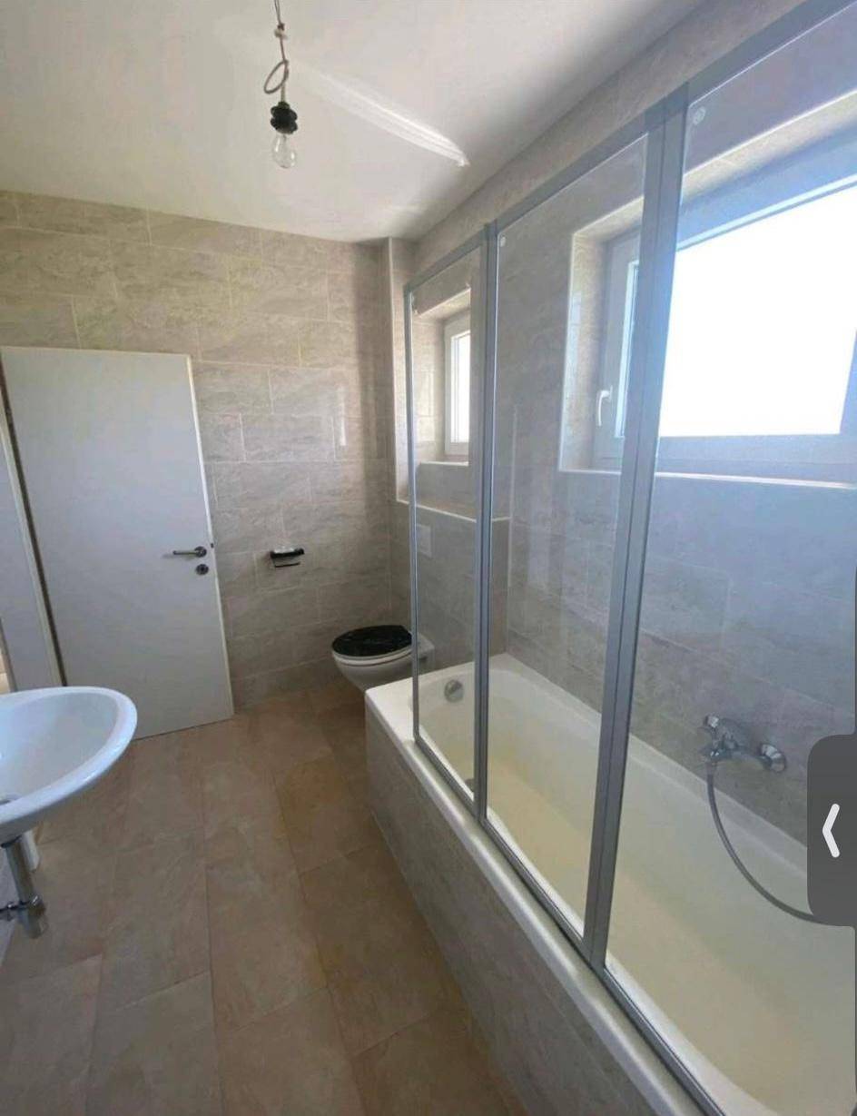 Helles Badezimmer mit Badewanne, Duschabtrennung und zwei Fenstern für Tageslicht.