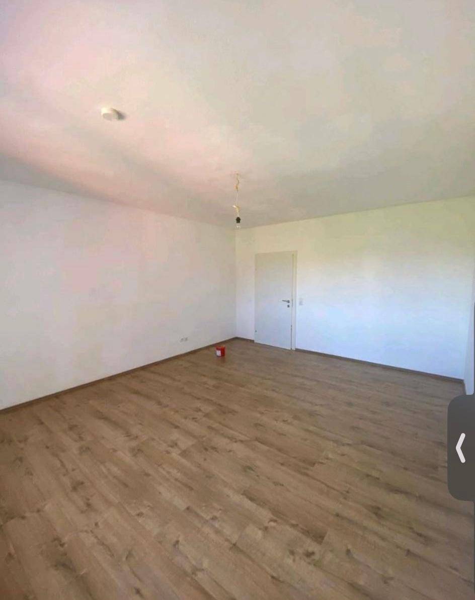 Helles, leeres Zimmer mit Laminatboden und weißen Wänden, bereit zur individuellen Gestaltung.
